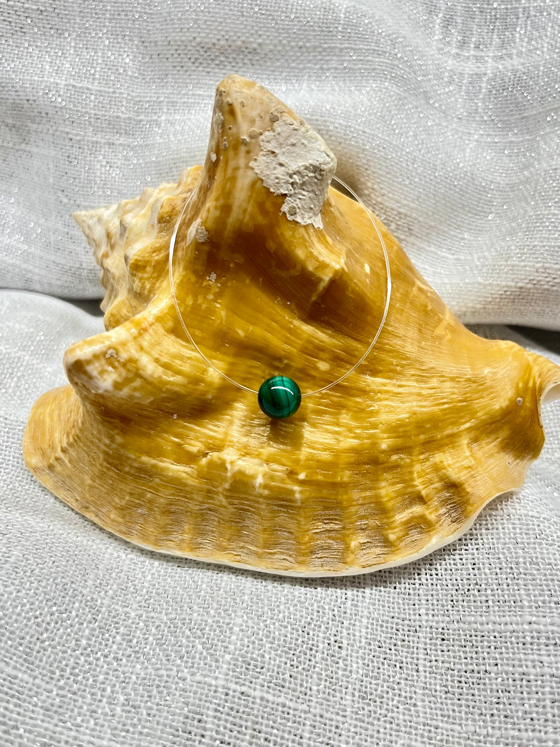 Collier EMY avec pierre de Malachite, exposé sur un coquillage.