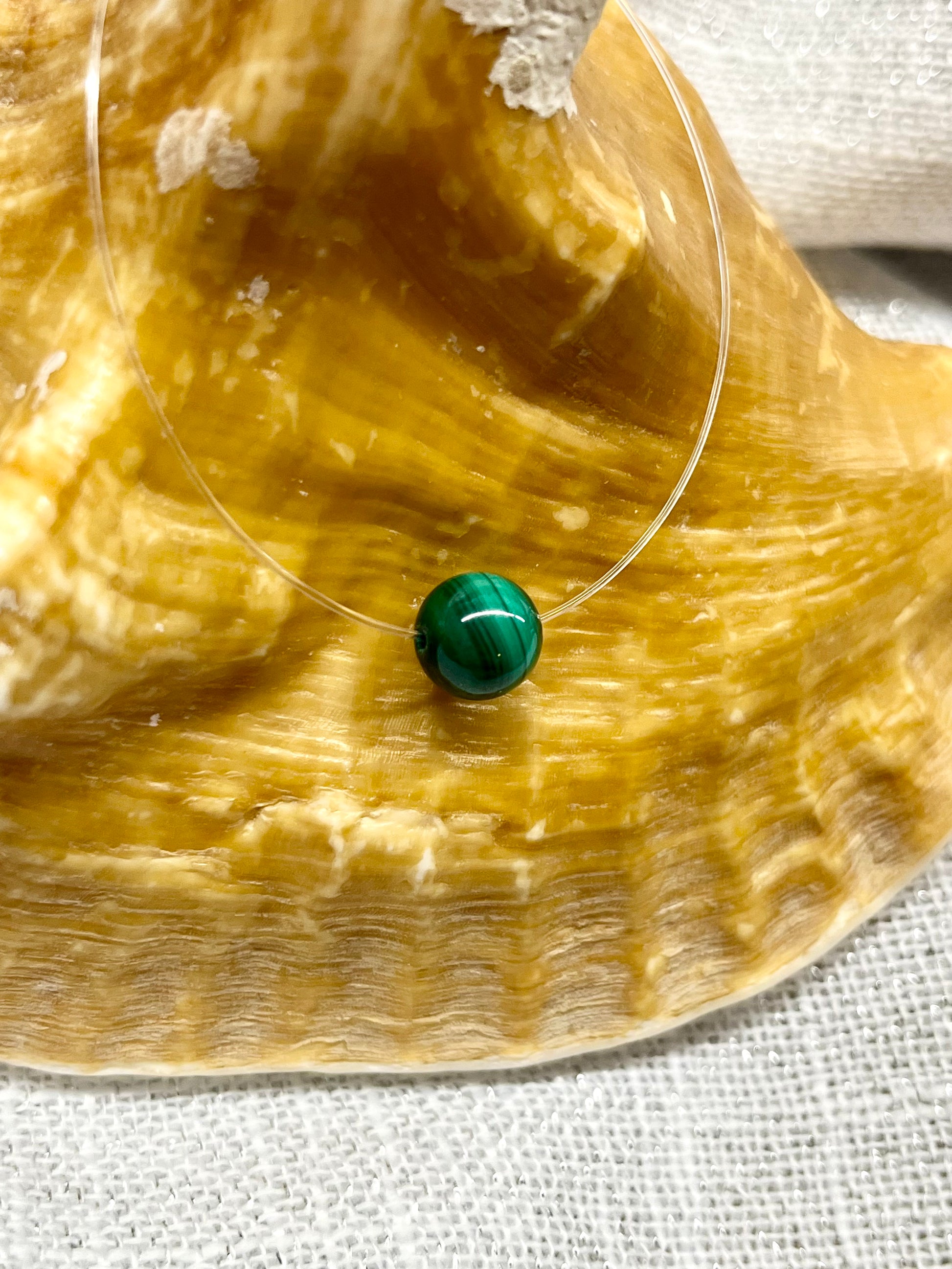 Collier EMY avec pierre de Malachite, exposé sur un coquillage.