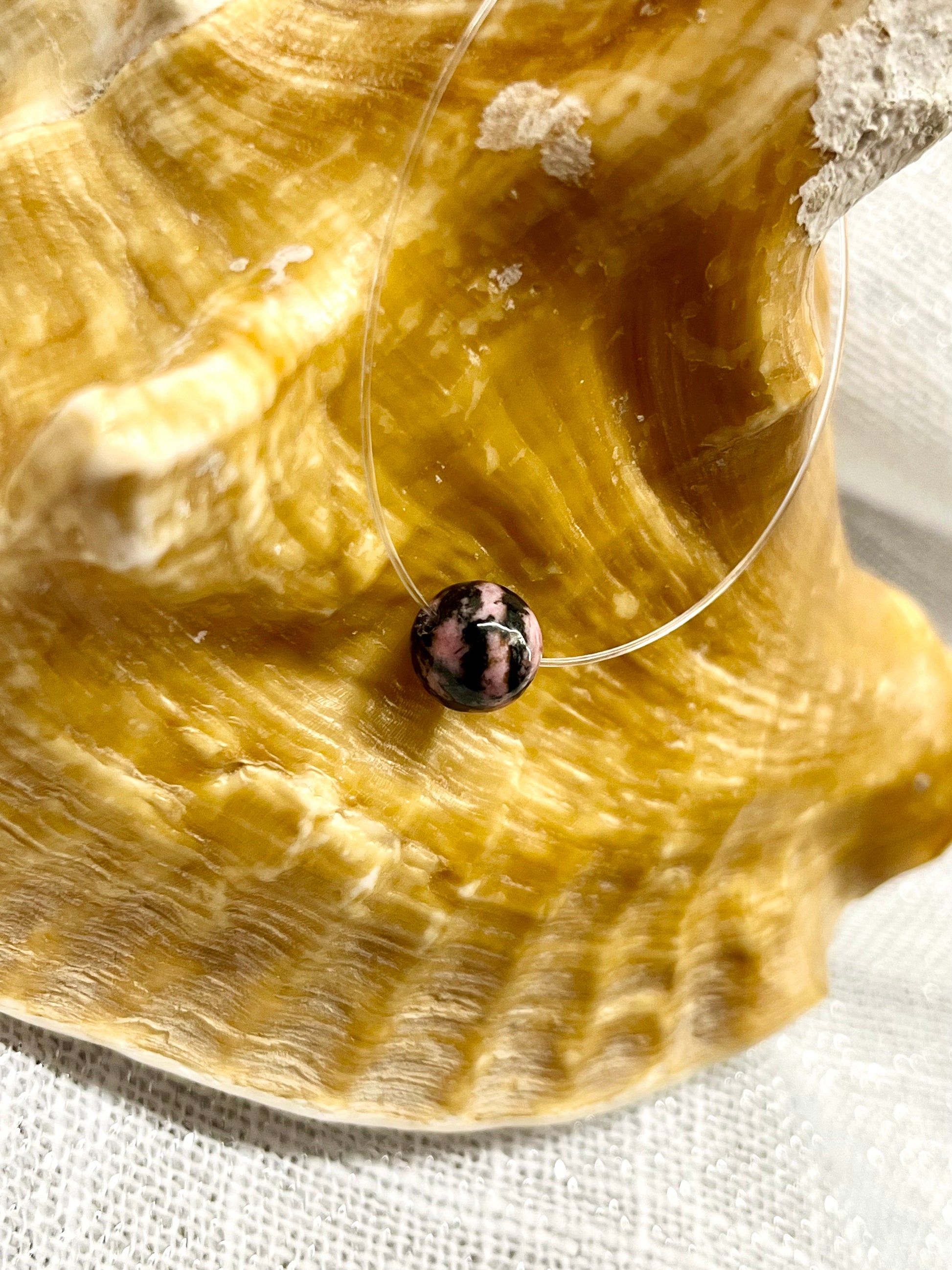 Collier EMY, avec pierre de Rhodonite, exposé sur un coquillage.