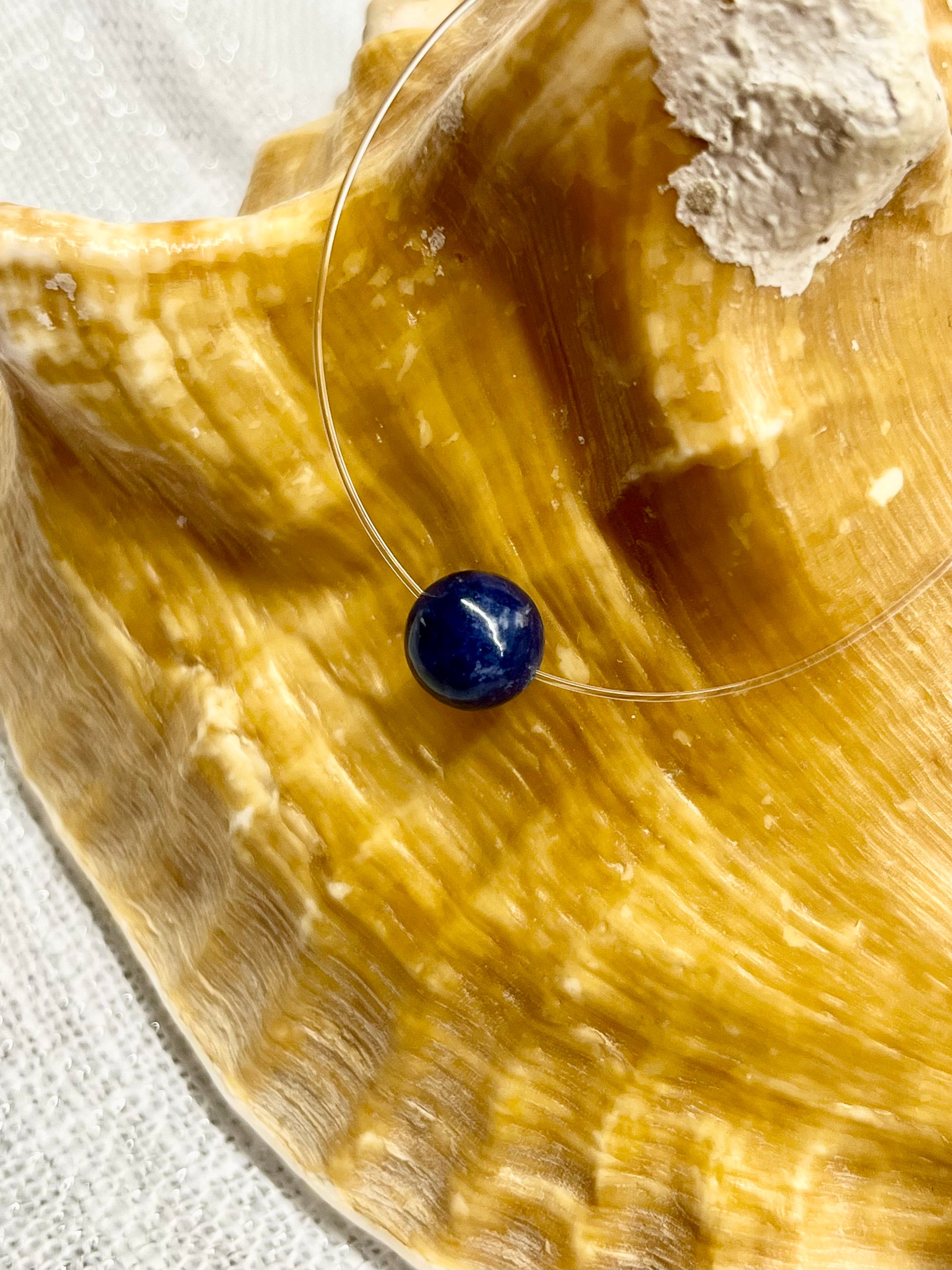 Collier EMY avec pierre de Sodalite, exposé sur un coquillage.