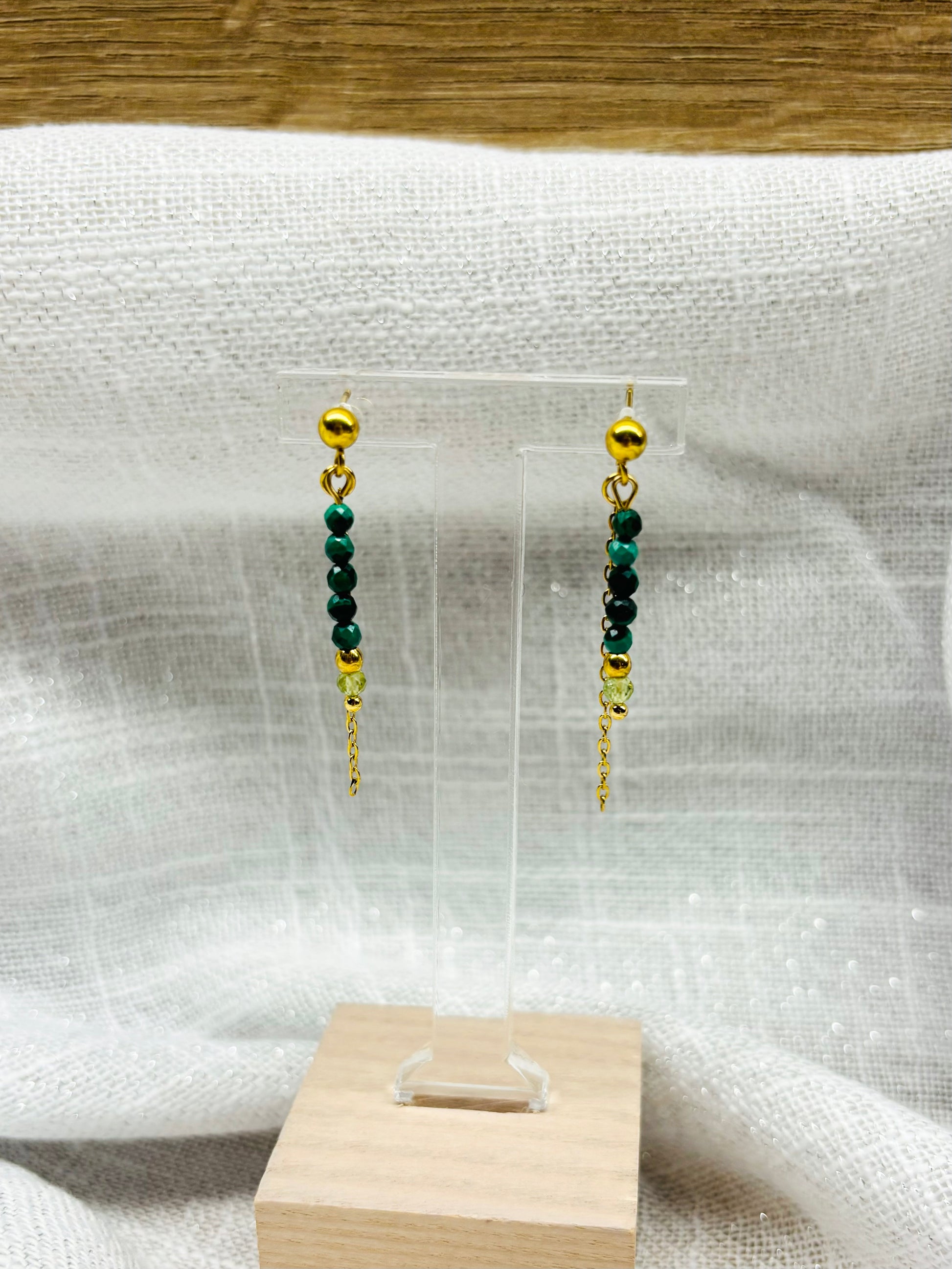 Boucles d'oreille JULIETTE, avec pierres de Malachite et de Péridot, exposées sur un fond en lin.