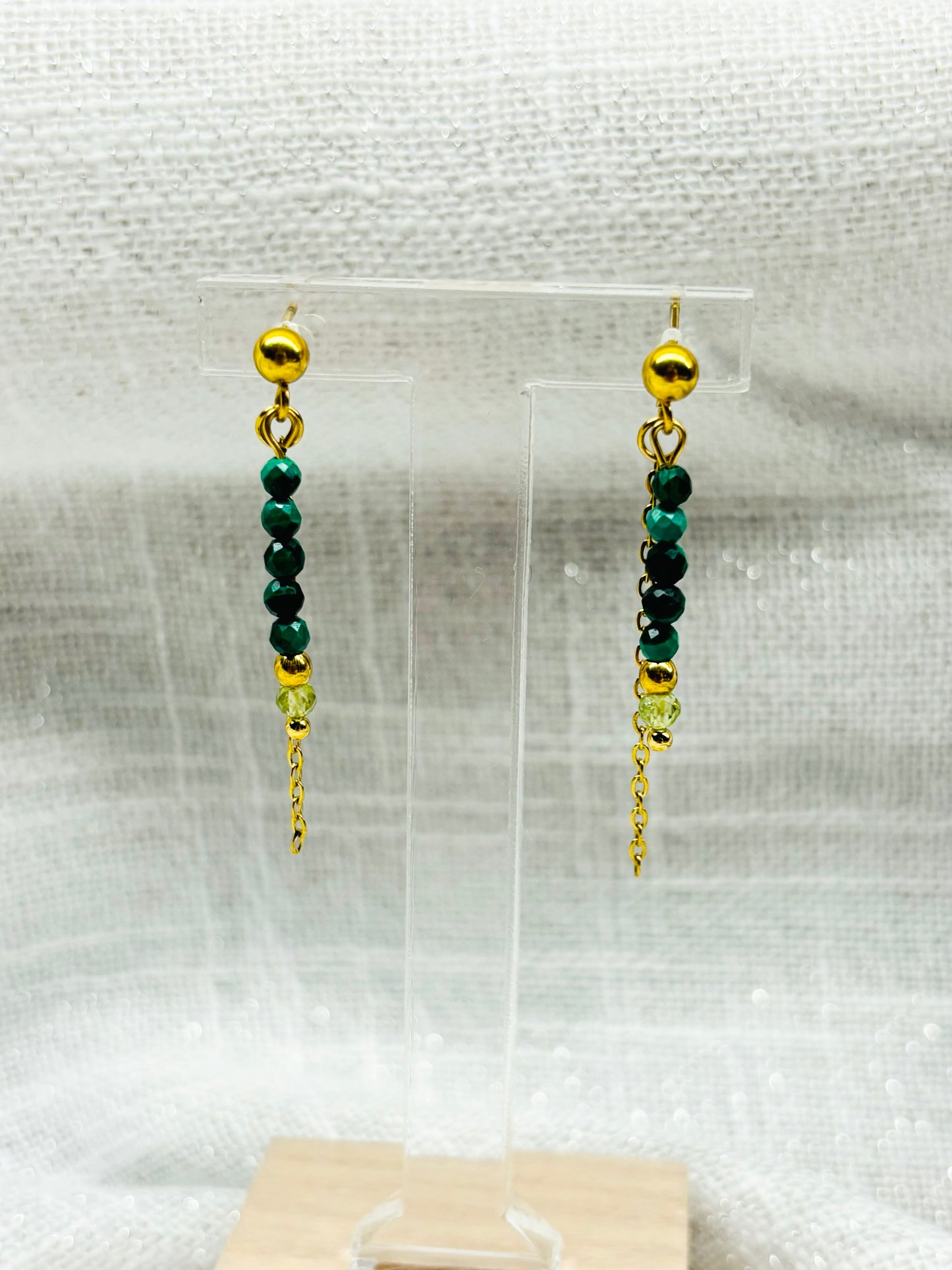 Boucles d'oreille JULIETTE, avec pierres de Malachite et de Péridot, exposées sur un fond en lin.