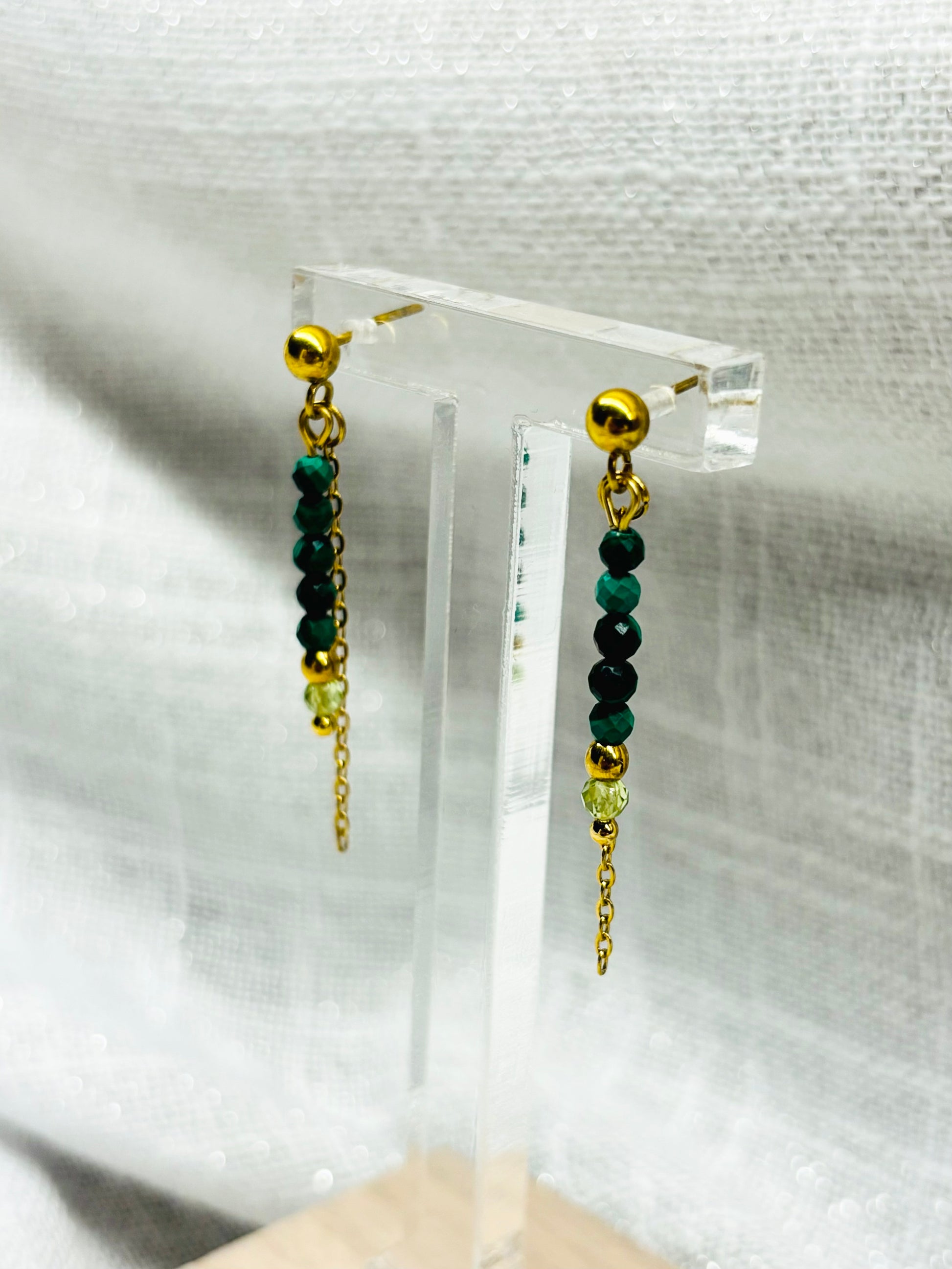 Boucles d'oreille JULIETTE, avec pierres de Malachite et de Péridot, exposées sur un fond en lin.