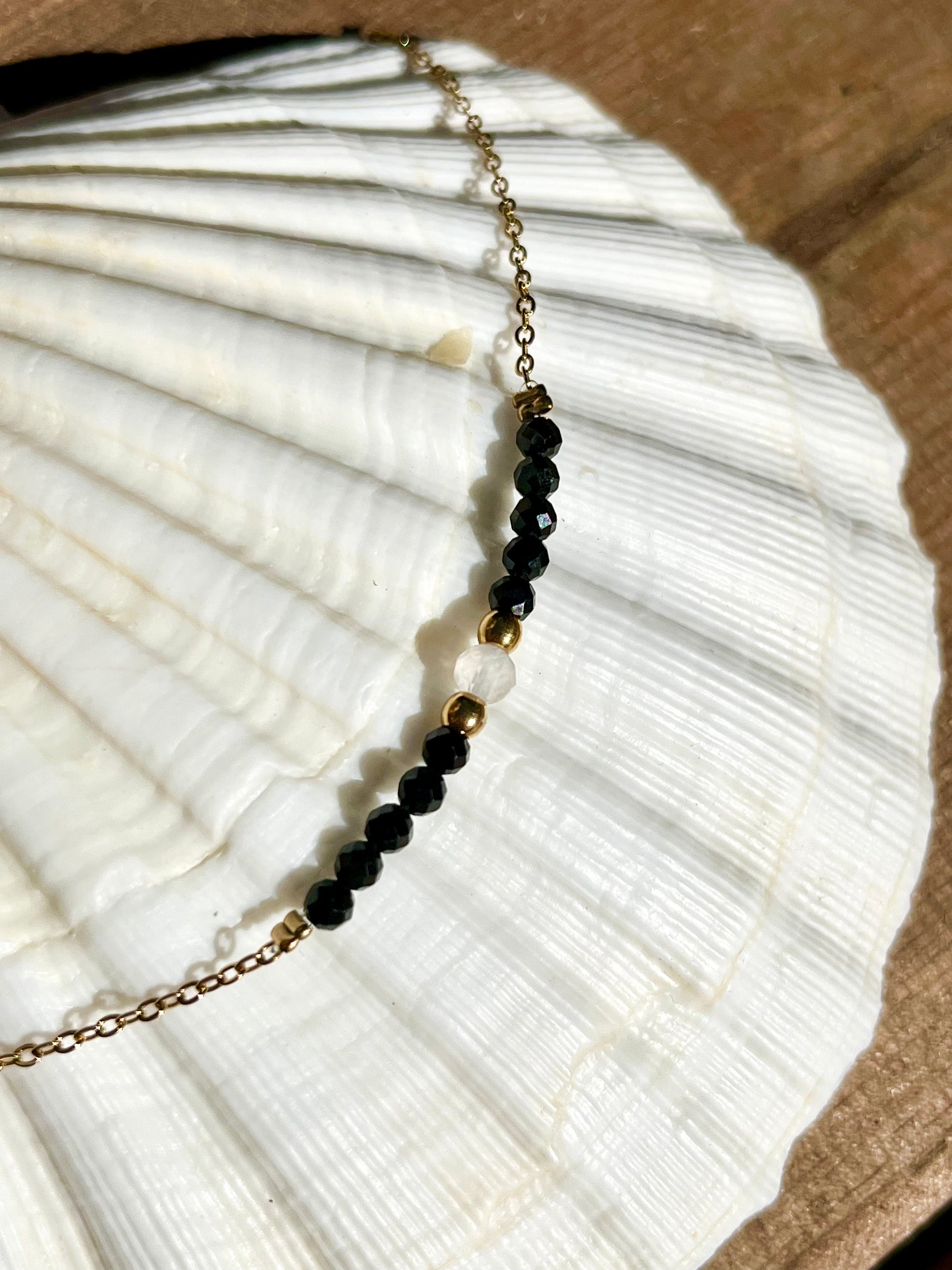 Collier JULIE, avec pierres de Tourmaline Noire et Pierre de Lune, exposé sur un coquillage.