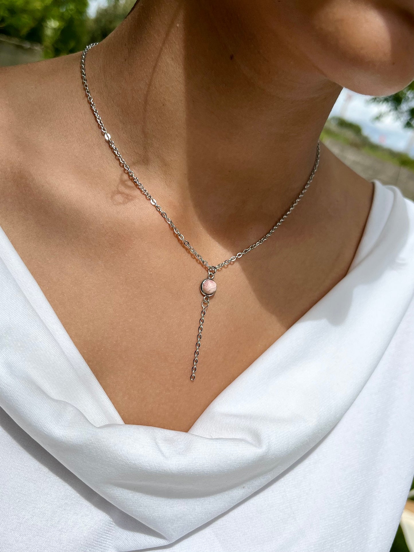 Collier LÉA, avec acier inoxydable argent et pierre de Rhodochrosite, porté par une femme sur un haut blanc.