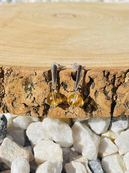 Boucles d'oreille MADELEINE, avec pierre de Citrine, exposées sur un rondin de bois.