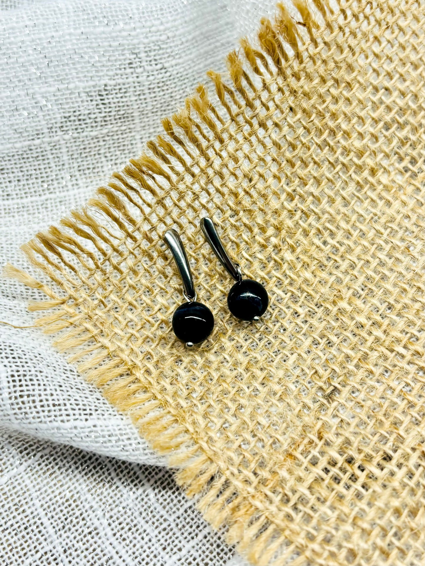 Boucles d'oreille MADELEINE, avec pierre d'Oeil de Faucon, exposées sur de la toile de jute.