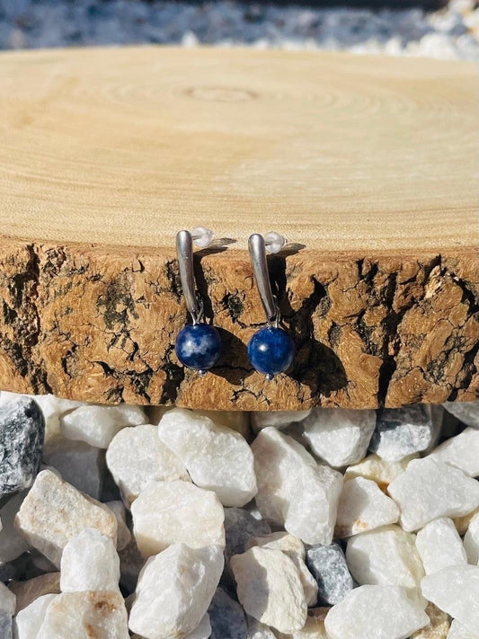 Boucles d'oreille MADELEINE, avec pierre de Sodalite, exposées sur un rondin de bois.