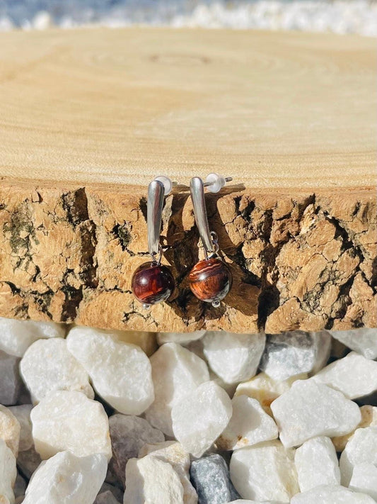 Boucles d'oreille MADELEINE, avec pierre d'Oeil de Taureau, exposées sur un rondin de bois.