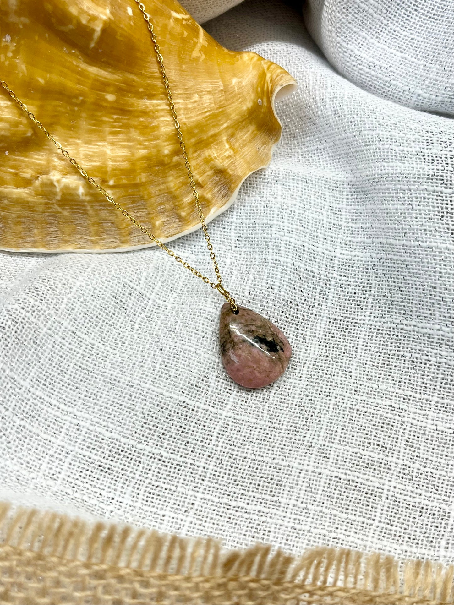 Collier MAELA, avec pierre de Rhodonite, exposé sur un fond en lin.