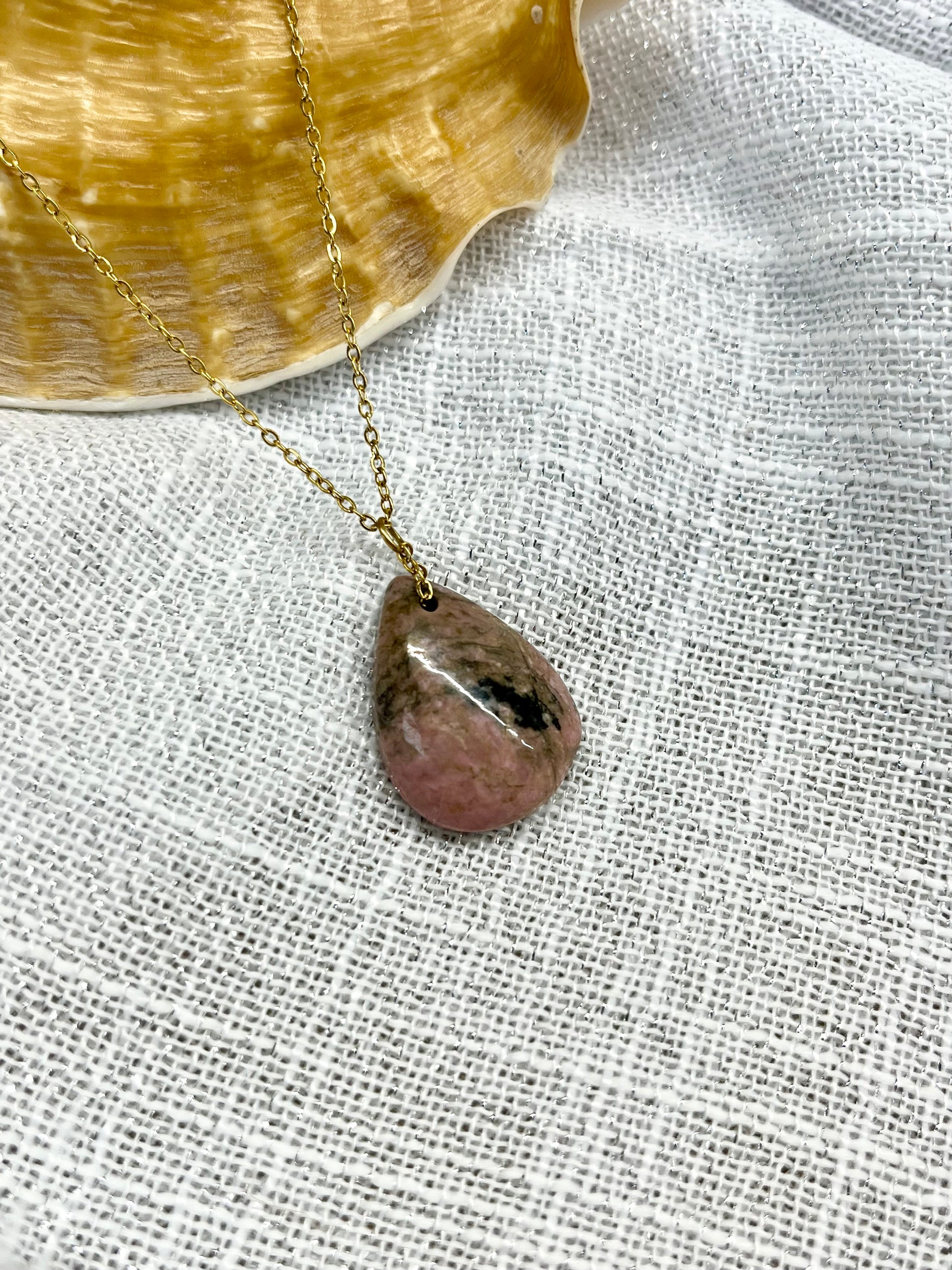 Collier MAELA, avec pierre de Rhodonite, exposé sur un fond en lin.