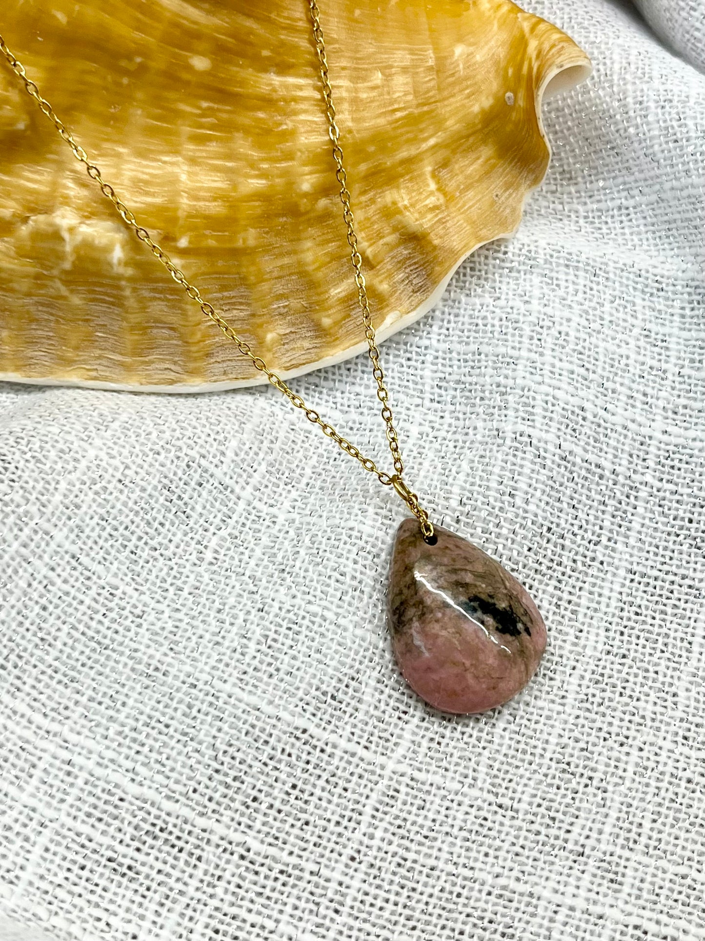 Collier MAELA, avec pierre de Rhodonite, exposé sur un fond en lin.