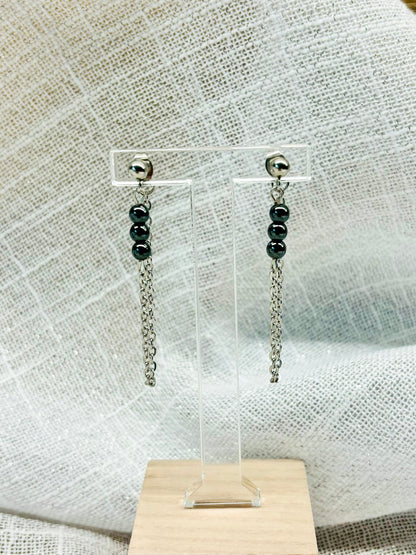 Boucles d'oreille MALIA, de couleur argent avec pierres d'hématite, exposées sur un fond en lin.