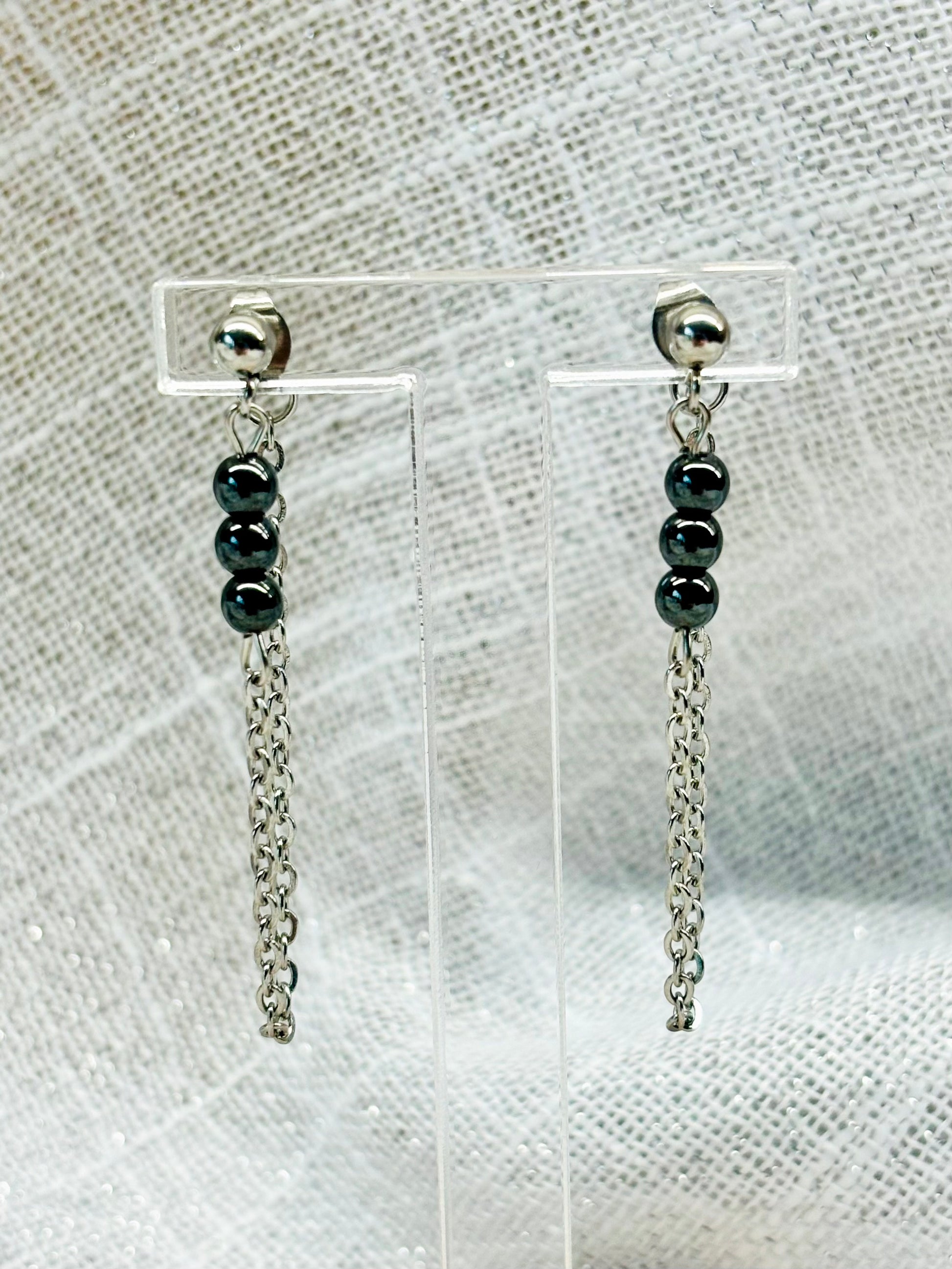 Boucles d'oreille MALIA, de couleur argent avec pierres d'hématite, exposées sur un fond en lin.