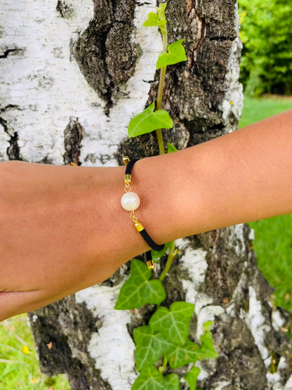 Bracelet MIA, avec cordon de couleur noir et perle de culture, porté sur un poignet de femme devant un arbre.