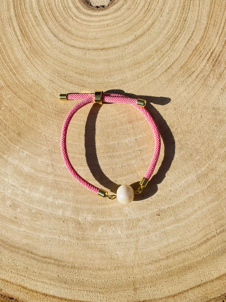 Bracelet MIA, avec cordon de couleur rose clair et perle de culture, exposé sur un fond en bois.