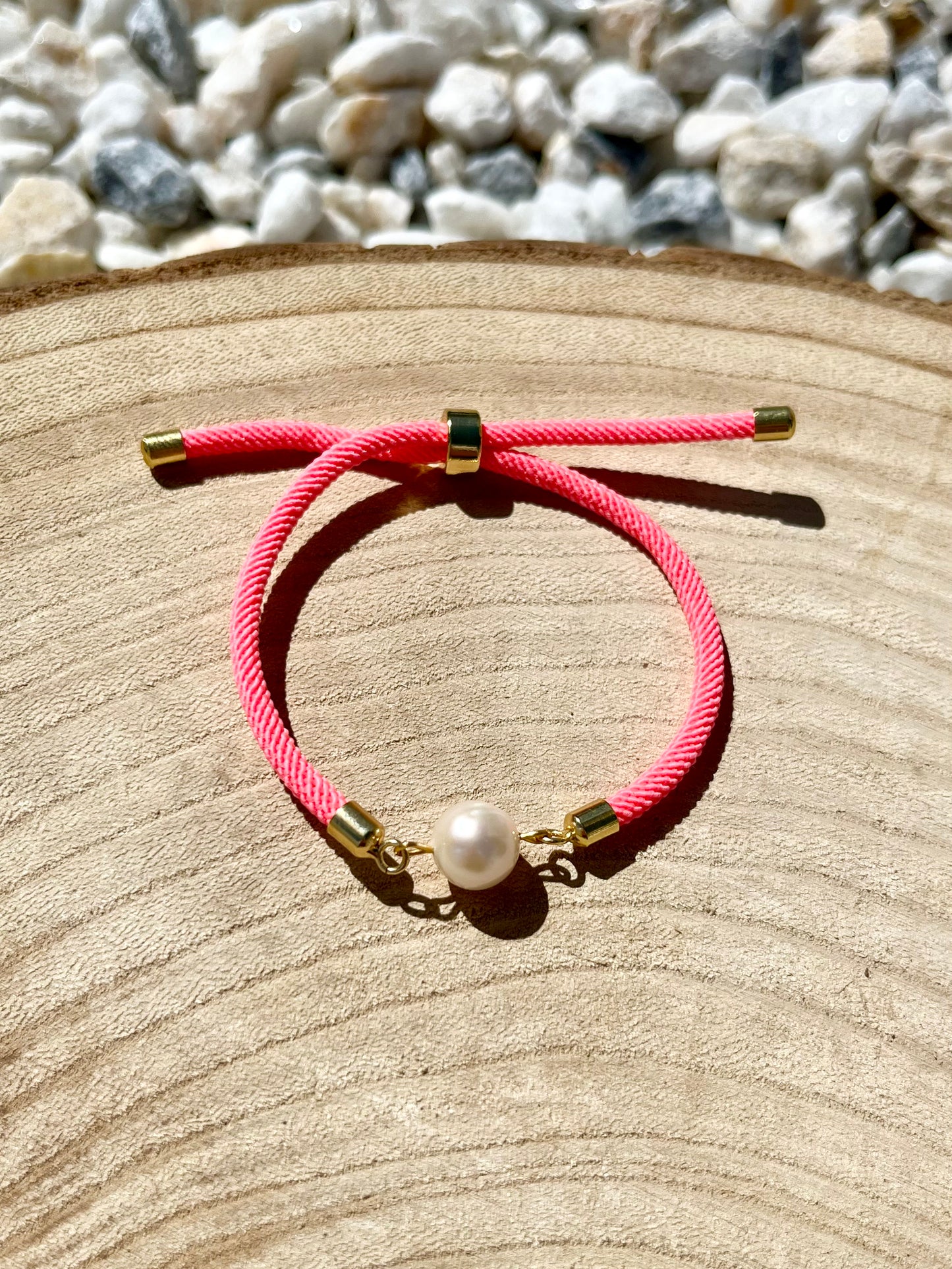 Bracelet MIA avec cordon de couleur rose fluo et perle de culture, exposé sur un fond en bois.