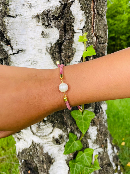 Bracelet MIA, avec cordon de couleur vieux rose et perle de culture, porté sur un poignet de femme devant un arbre.