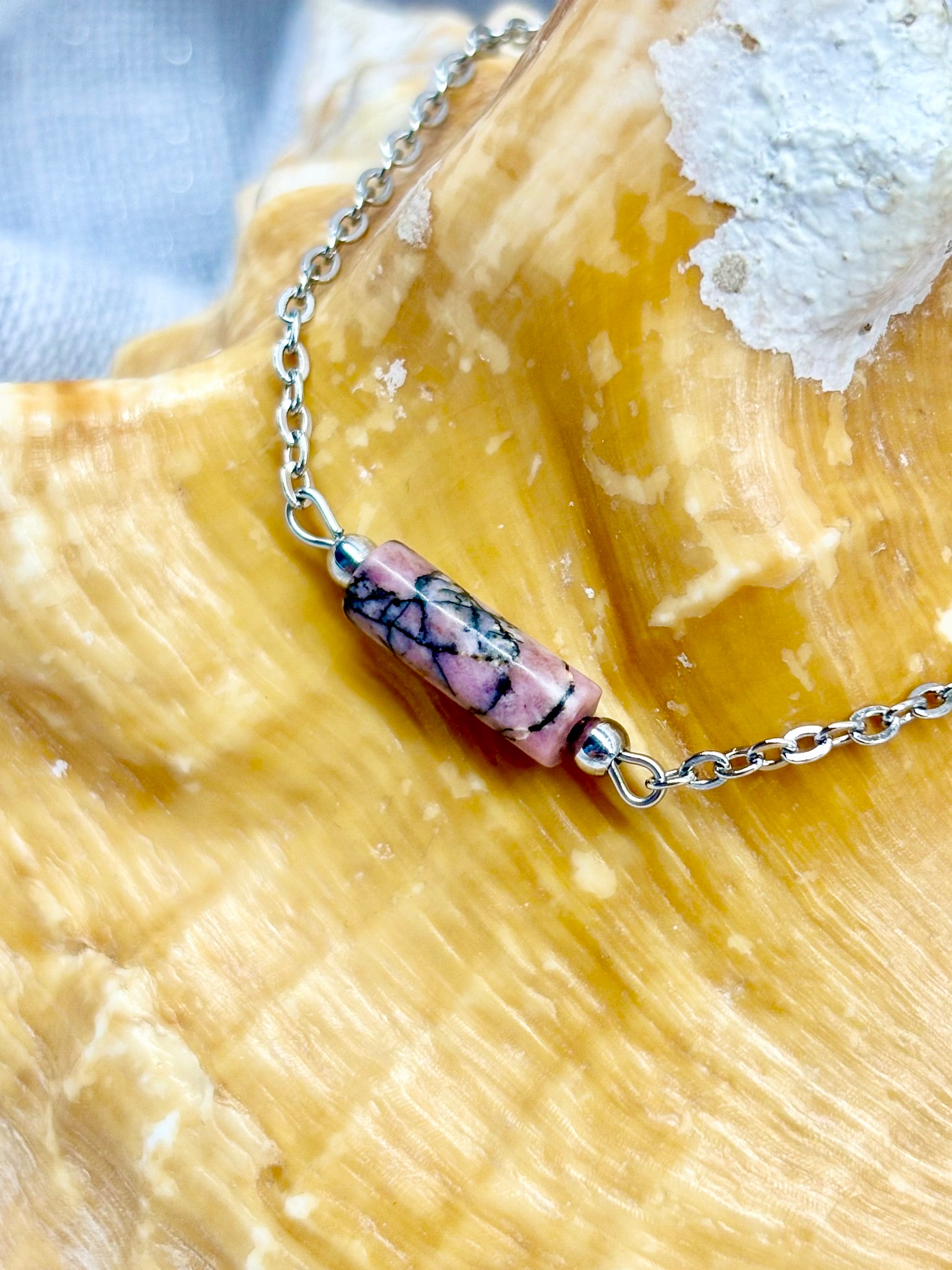 Bracelet NORA, avec pierre de Rhodochrosite, exposé sur un coquillage.