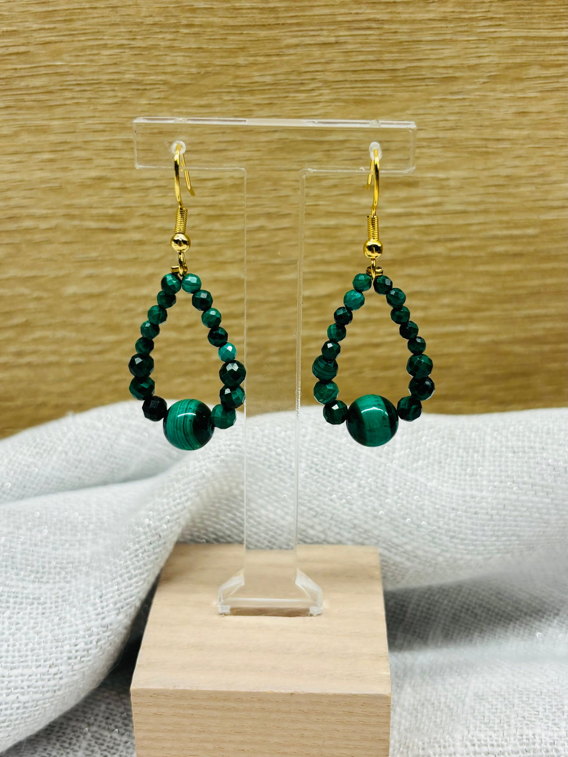 Boucles d'oreille SIMONA, avec pierres de Malachite, exposées devant un fond en bois.