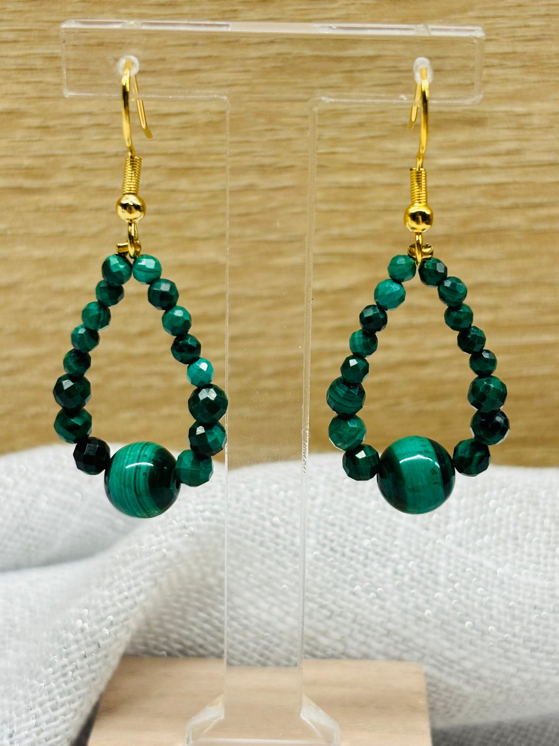 Boucles d'oreille SIMONA, avec pierres de Malachite, exposées devant un fond en bois.