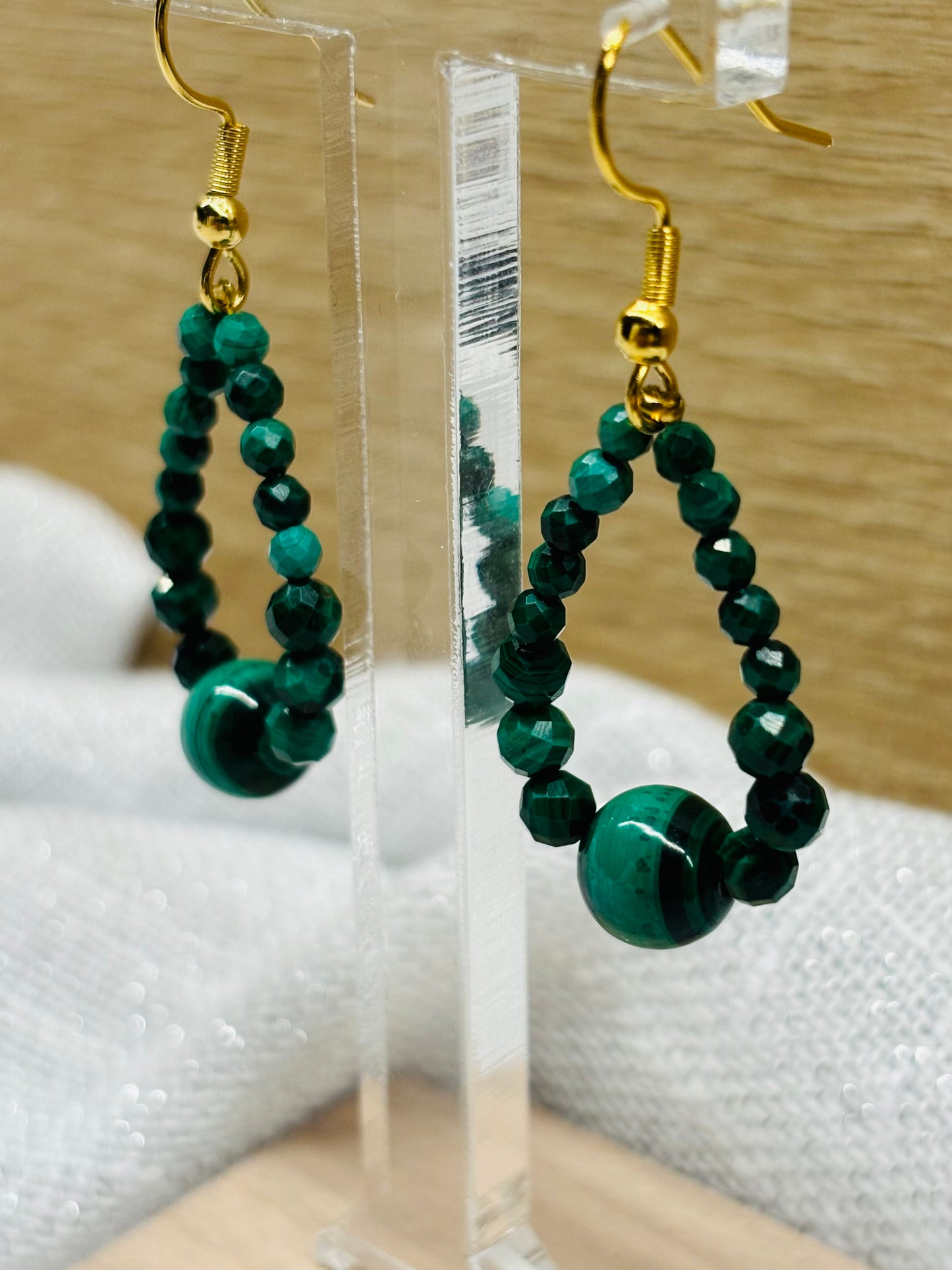 Boucles d'oreille SIMONA, avec pierres de Malachite, exposées devant un fond en bois.