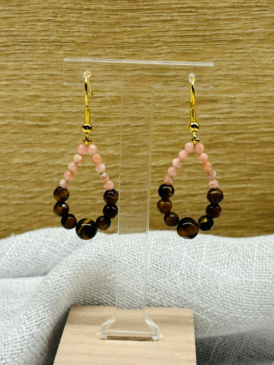 Boucles d'oreille SIMONA, avec pierres d'Oeil de Tigre et de Rhodochrosite, exposées devant un fond en bois.