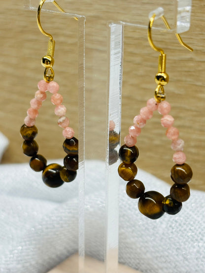 Boucles d'oreille SIMONA, avec pierres d'Oeil de Tigre et de Rhodochrosite, exposées devant un fond en bois.