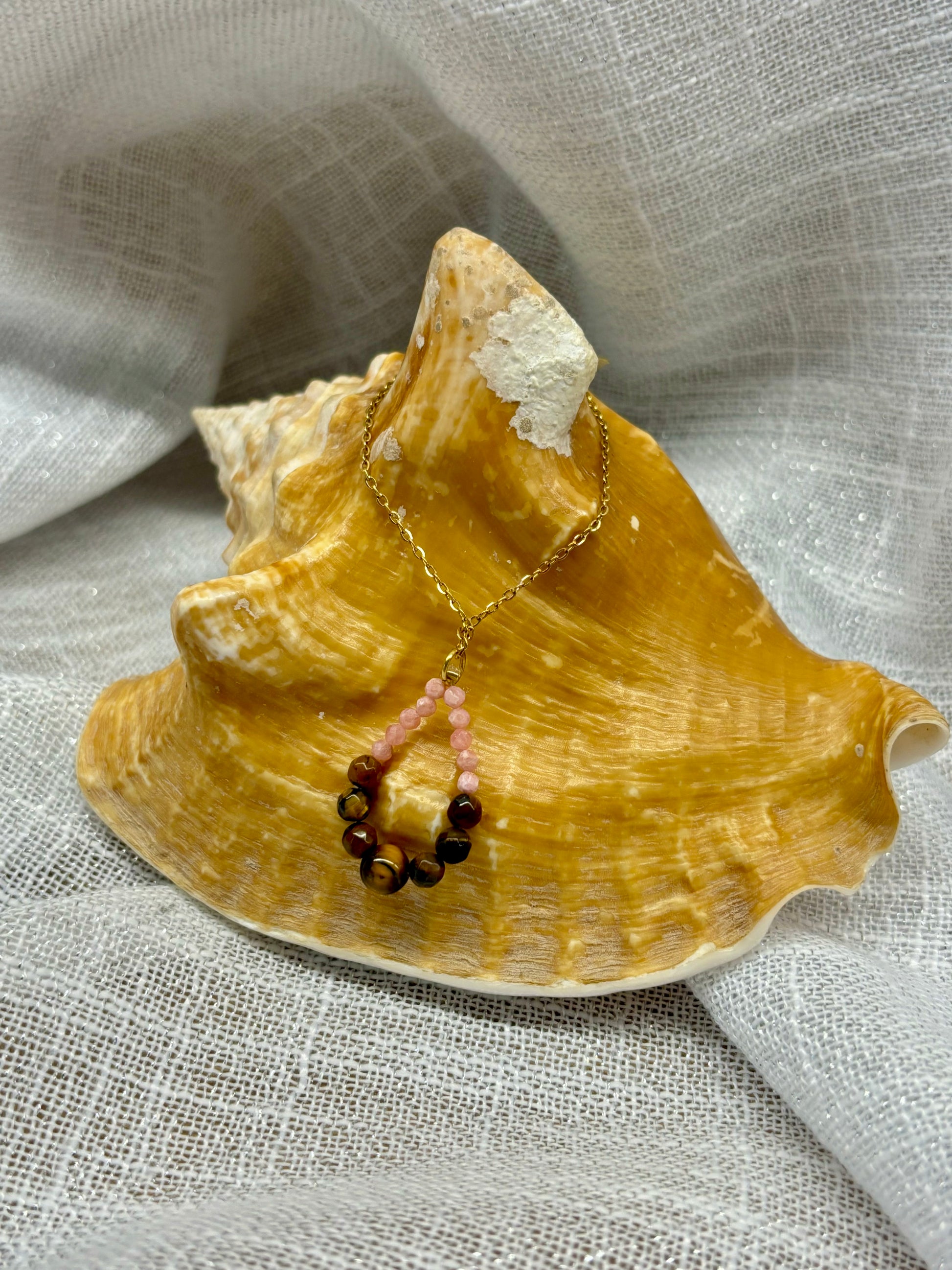 Collier SIMONA, avec pierres d'Oeil de Tigre et Rhodochrosite, exposé sur un coquillage.