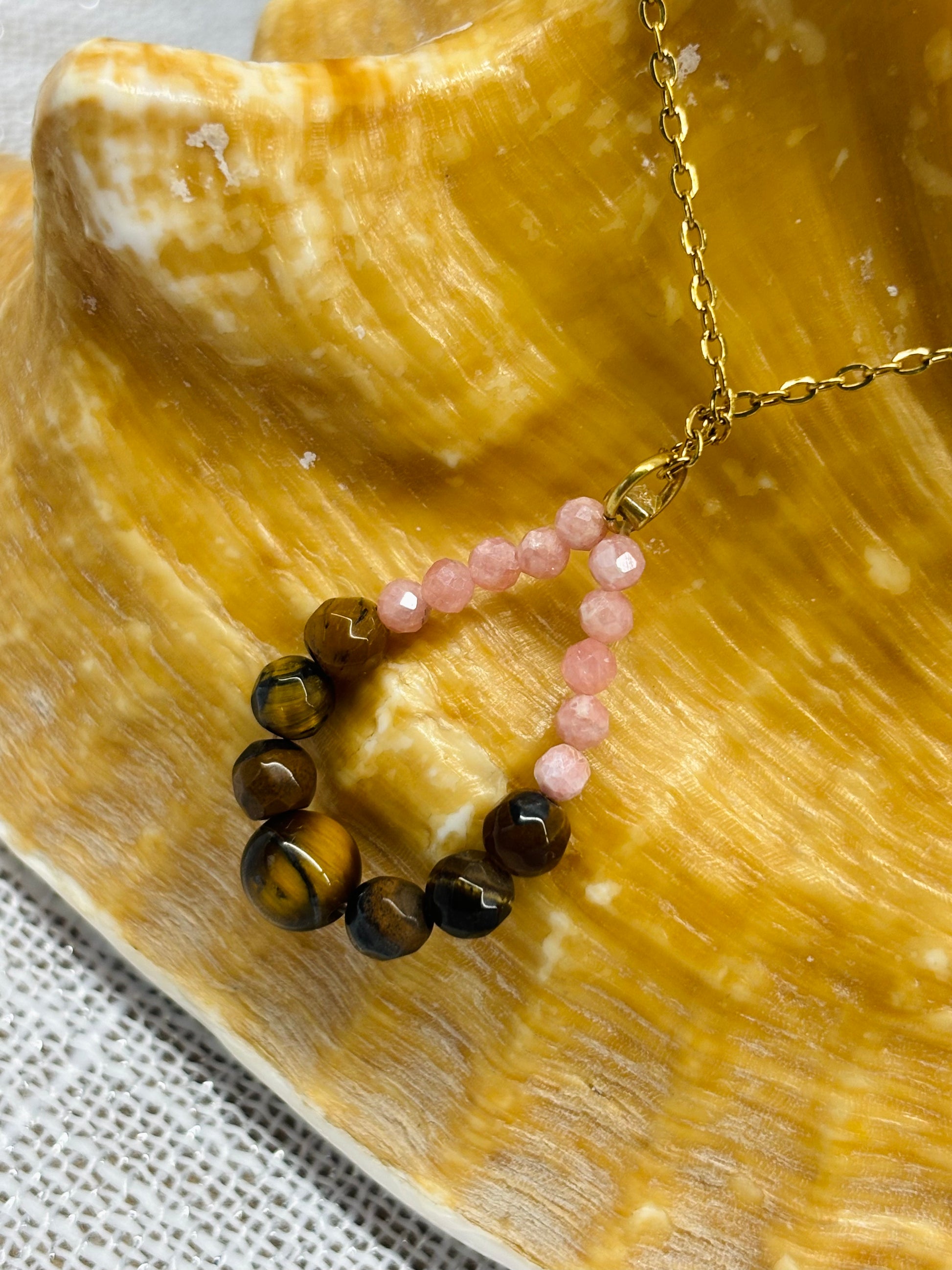 Collier SIMONA, avec pierres d'Oeil de Tigre et Rhodochrosite, exposé sur un coquillage.