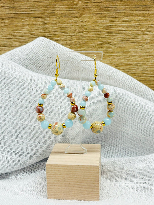 Boucles d'oreille SIMONE, avec pierres de Jaspe Aqua Terra, exposées devant un fond en bois et en lin.