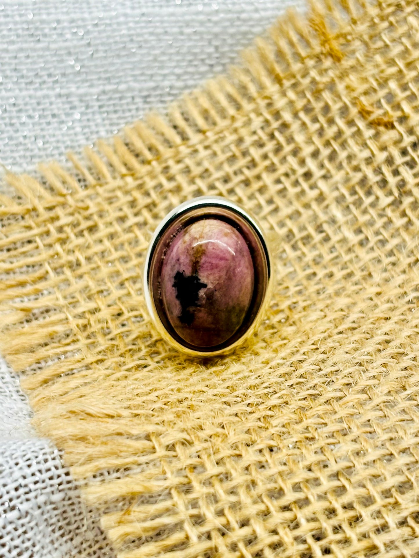 Bague THÉA, en argent et pierre de Rhodonite, sur un fond en lin et toile de jute.