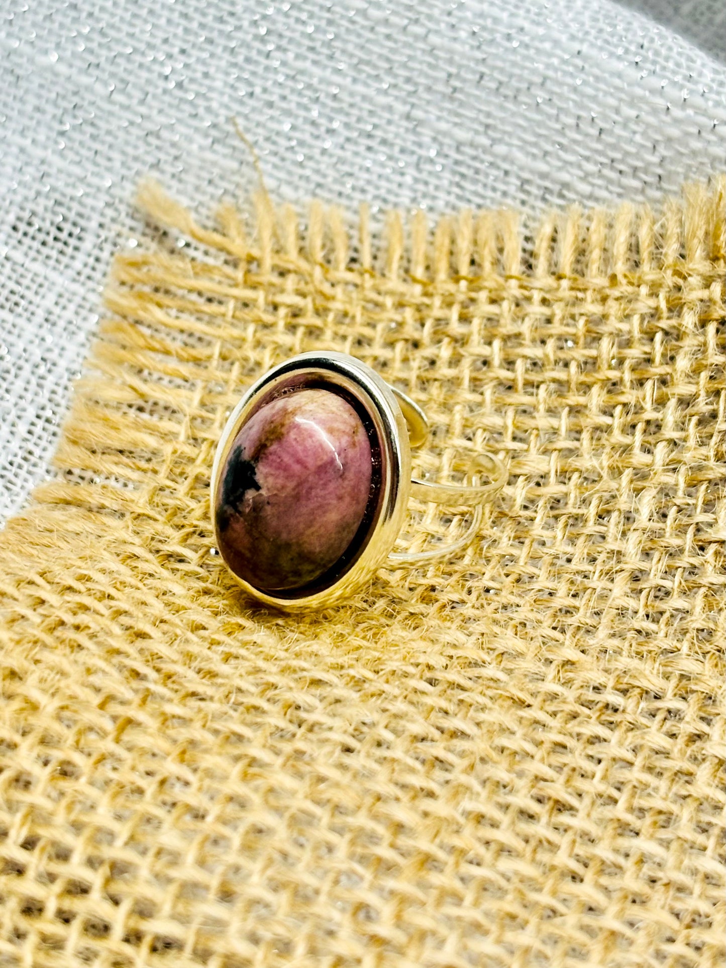 Bague THÉA, en argent et pierre de Rhodonite, sur un fond en lin et toile de jute.