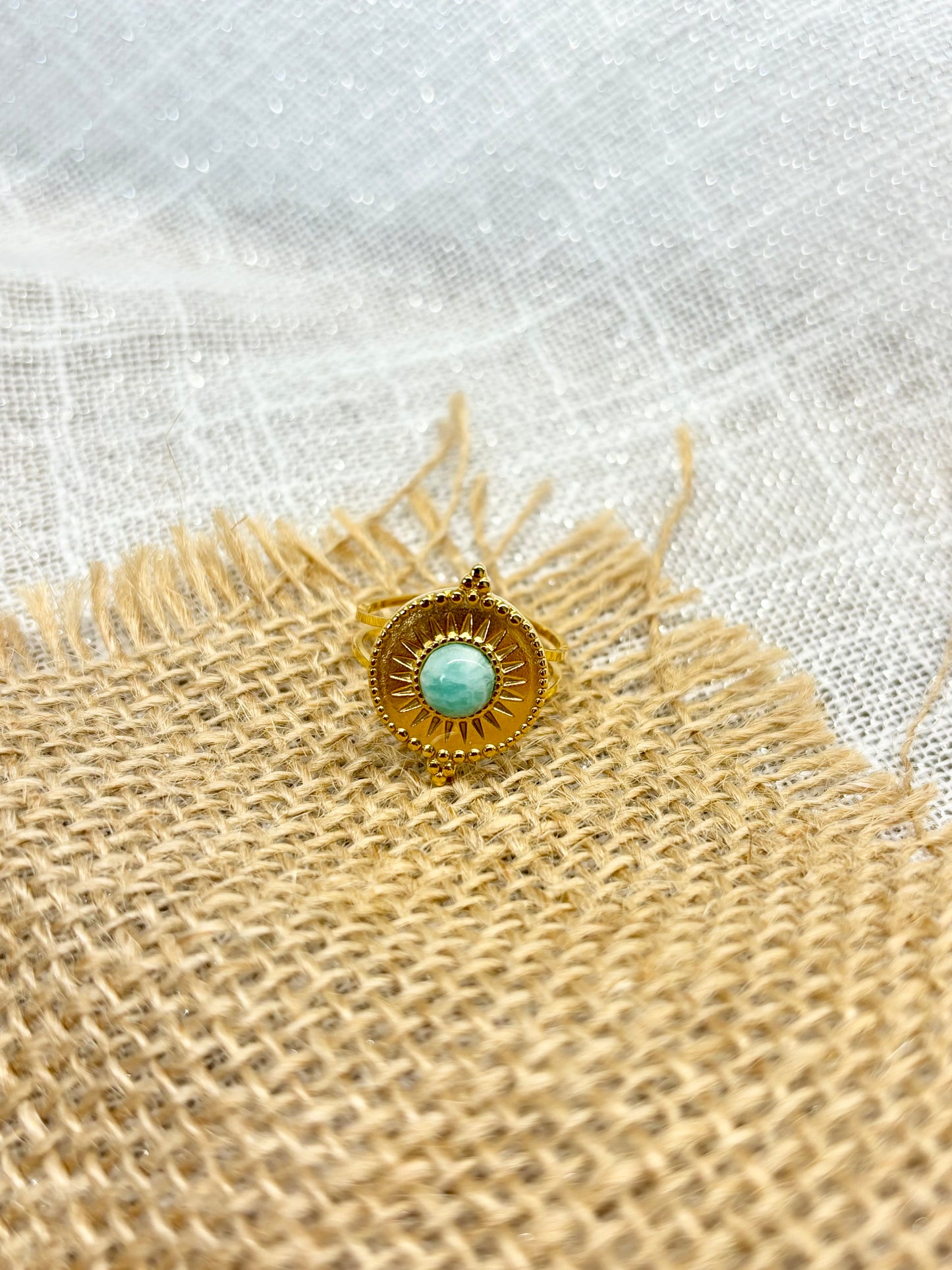 Bague ZÉLIE, en acier inoxydable doré et pierre d'amazonite, exposé sur du lin et de la jute.