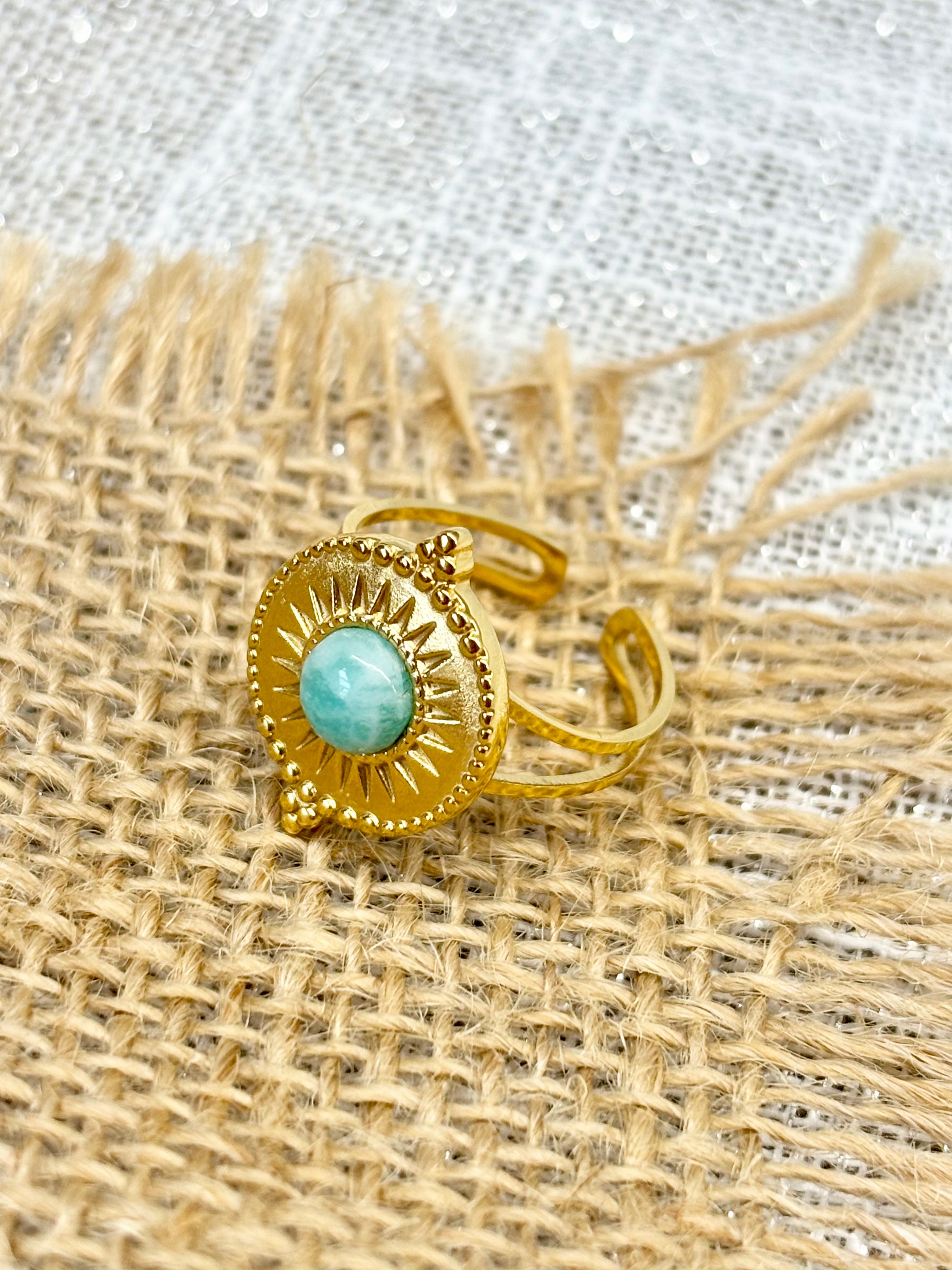 Bague ZÉLIE, en acier inoxydable doré et pierre d'amazonite, exposé sur du lin et de la jute.