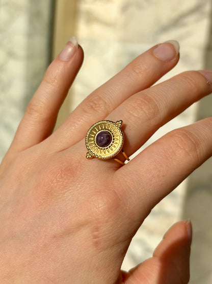 Bague ZÉLIE, en acier inoxydable doré et pierre d'Améthyste, portée sur une main de femme.