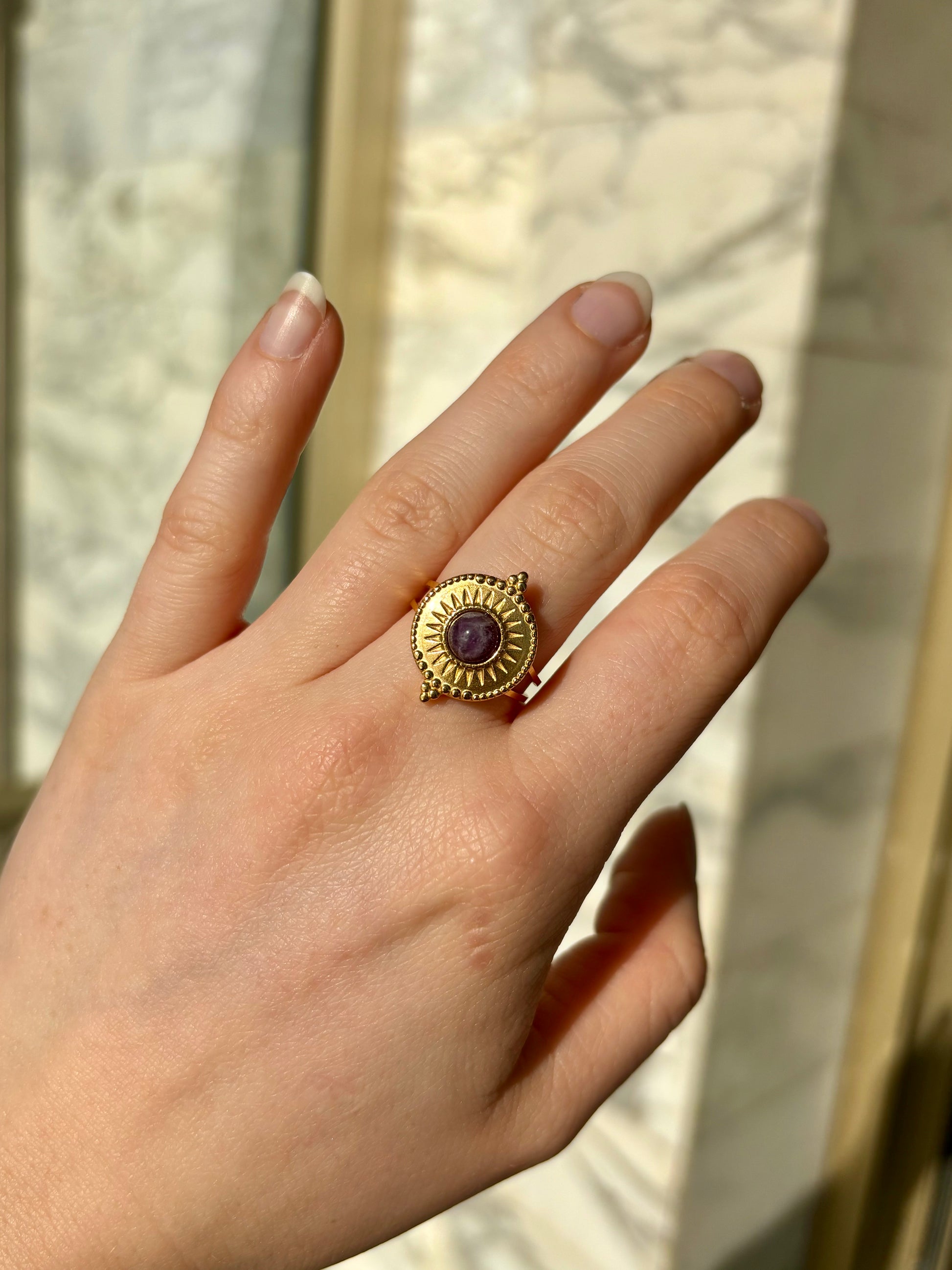 Bague ZÉLIE, en acier inoxydable doré et pierre d'Améthyste, portée sur une main de femme.