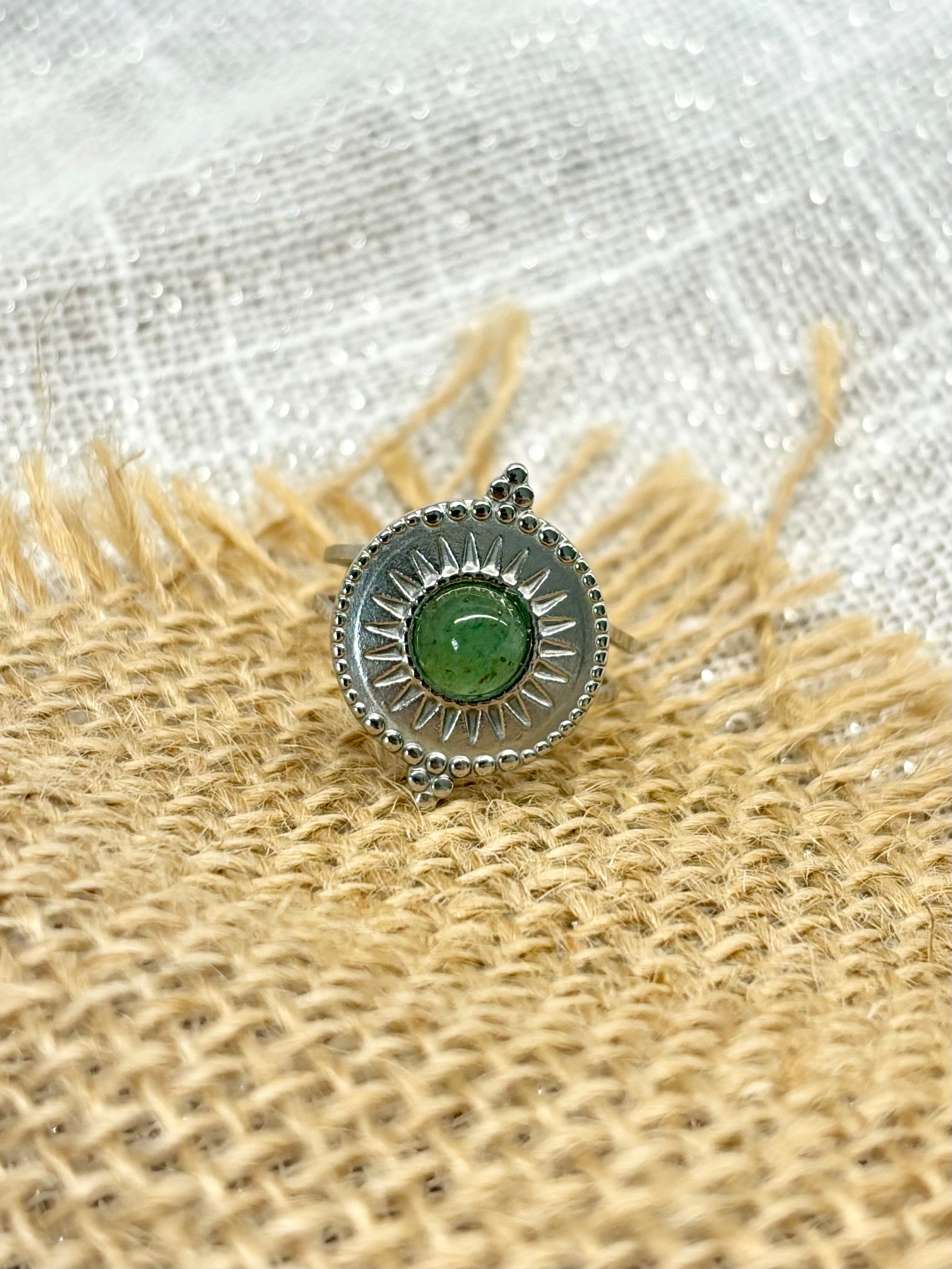 Bague ZÉLIE en acier inoxydable argent, avec pierre d'Aventurine, exposée sur de la toile de jute et fond en lin blanc.