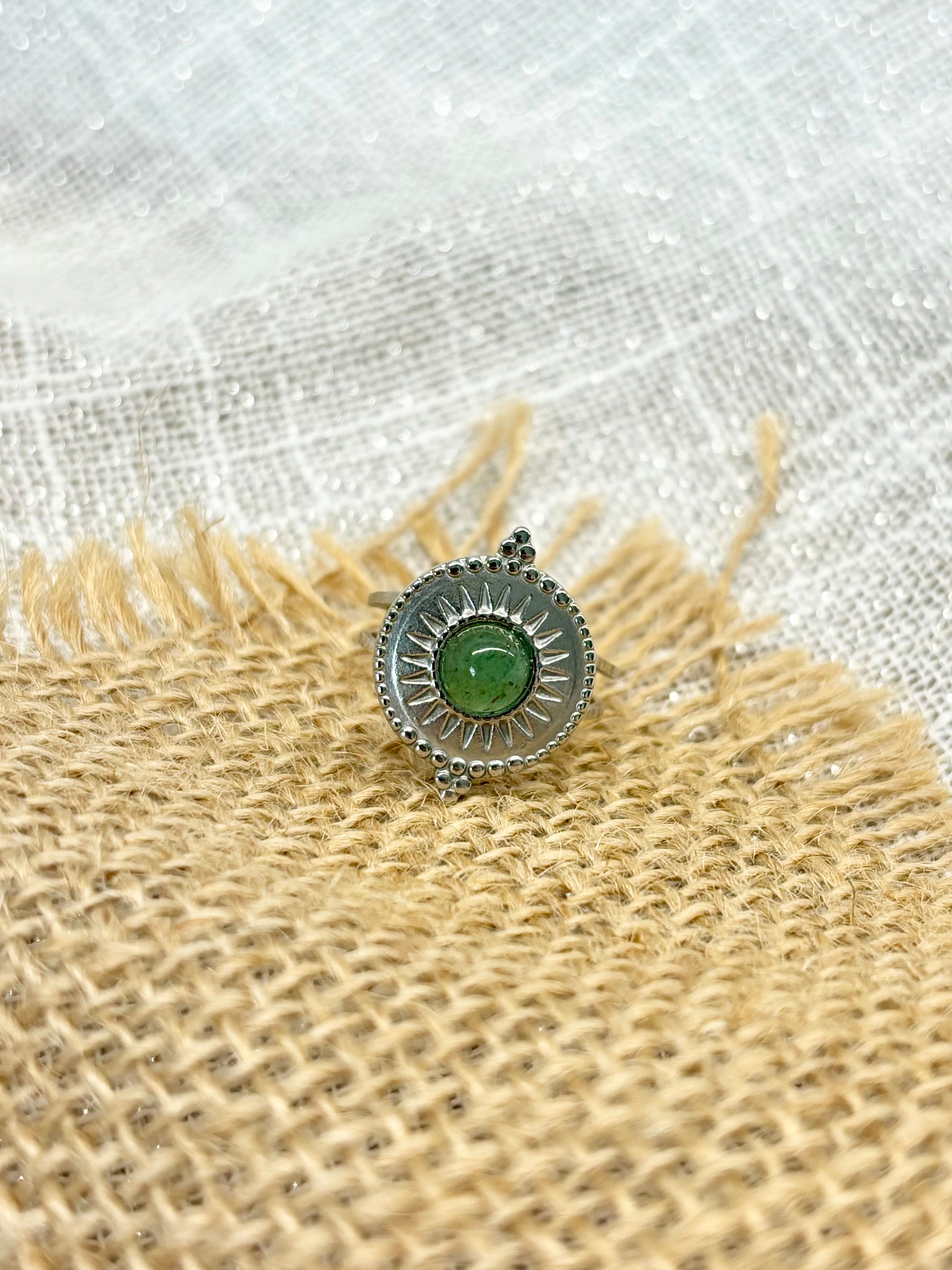 Bague ZÉLIE en acier inoxydable argent, avec pierre d'Aventurine, exposée sur de la toile de jute et fond en lin blanc.