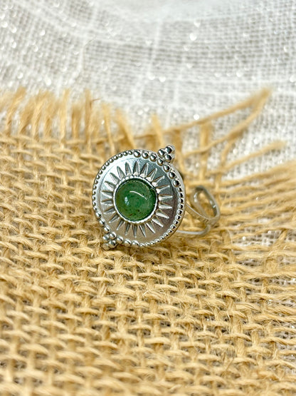 Gros plan de la Bague ZÉLIE en acier inoxydable argent, avec pierre d'Aventurine, exposée sur de la toile de jute et fond en lin blanc.