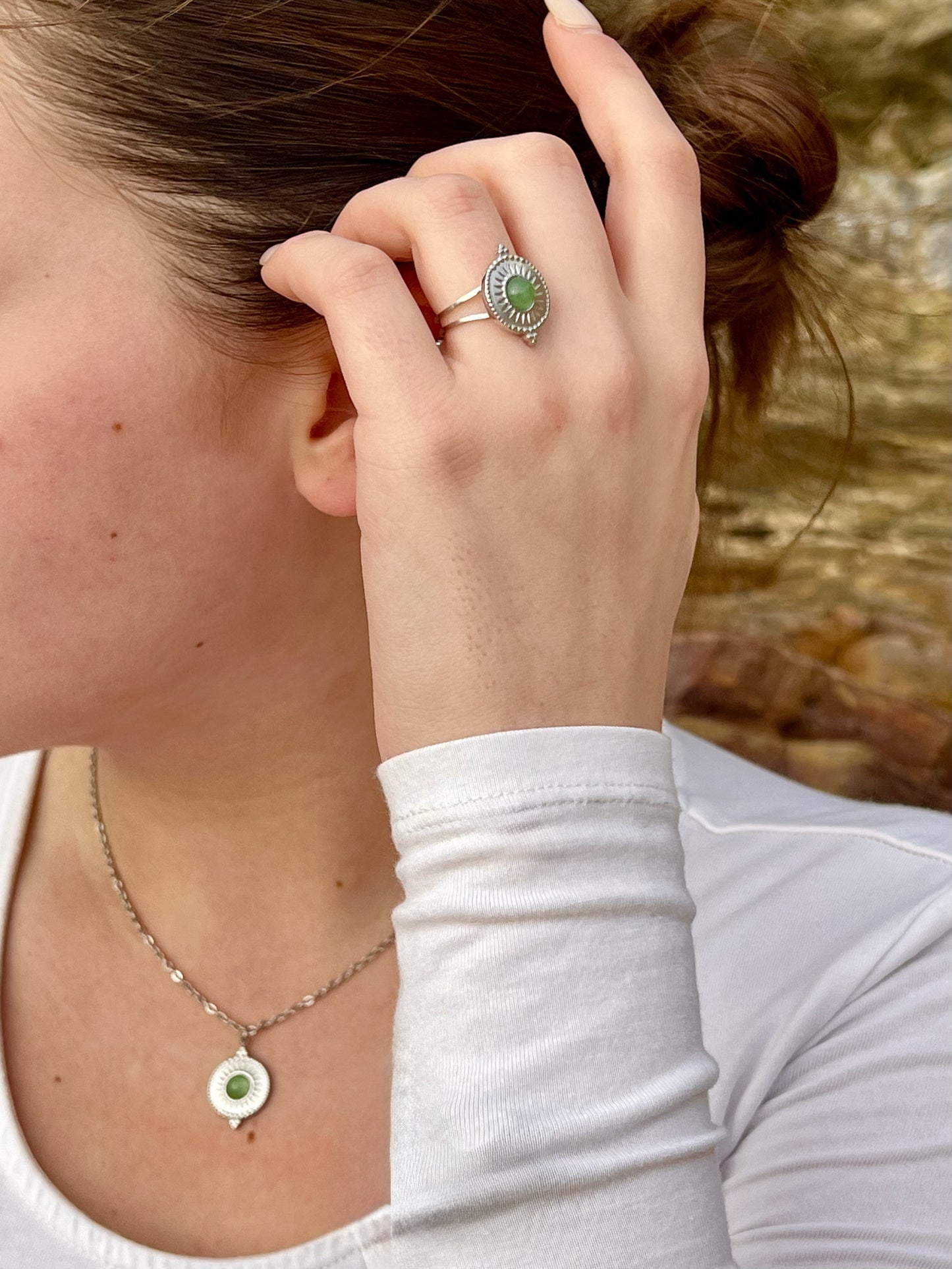 Bague et collier ZÉLIE en acier inoxydable argent, avec pierre d'Aventurine, portée par une femme dans les rochers.