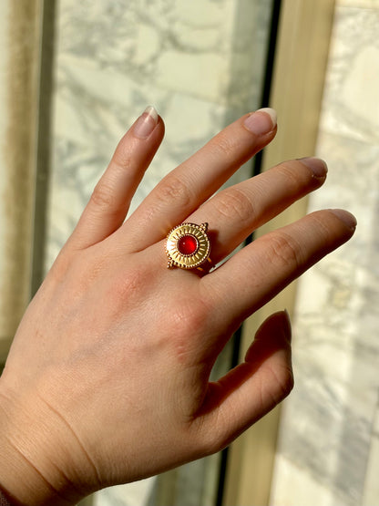 Bague ZÉLIE en acier inoxydable doré, avec pierre de cornaline, portée sur une main de femme avec un fond en marbre.