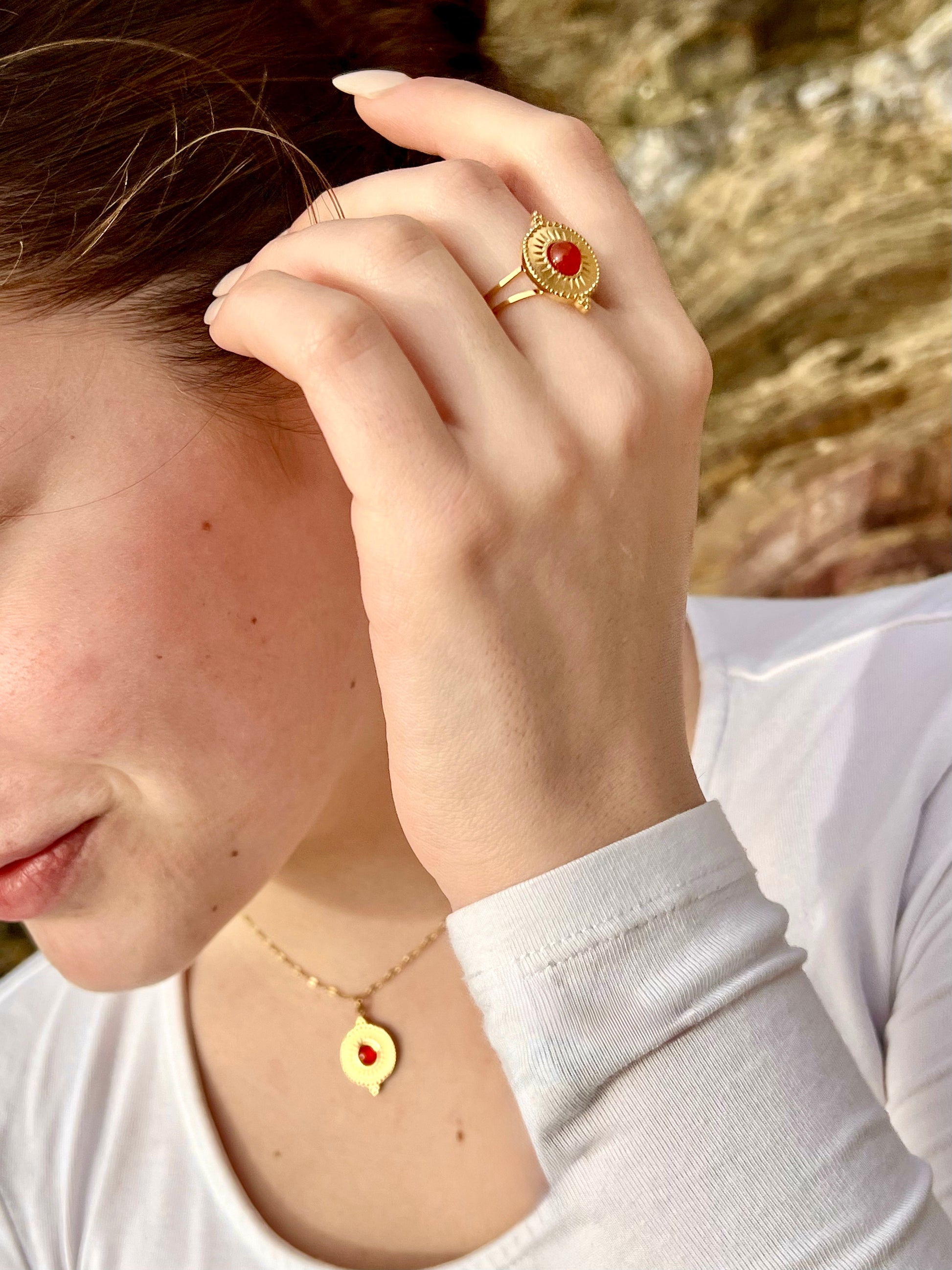 Bague et collier ZÉLIE en acier inoxydable doré, avec pierre de cornaline, portée par une femme dans les rochers.