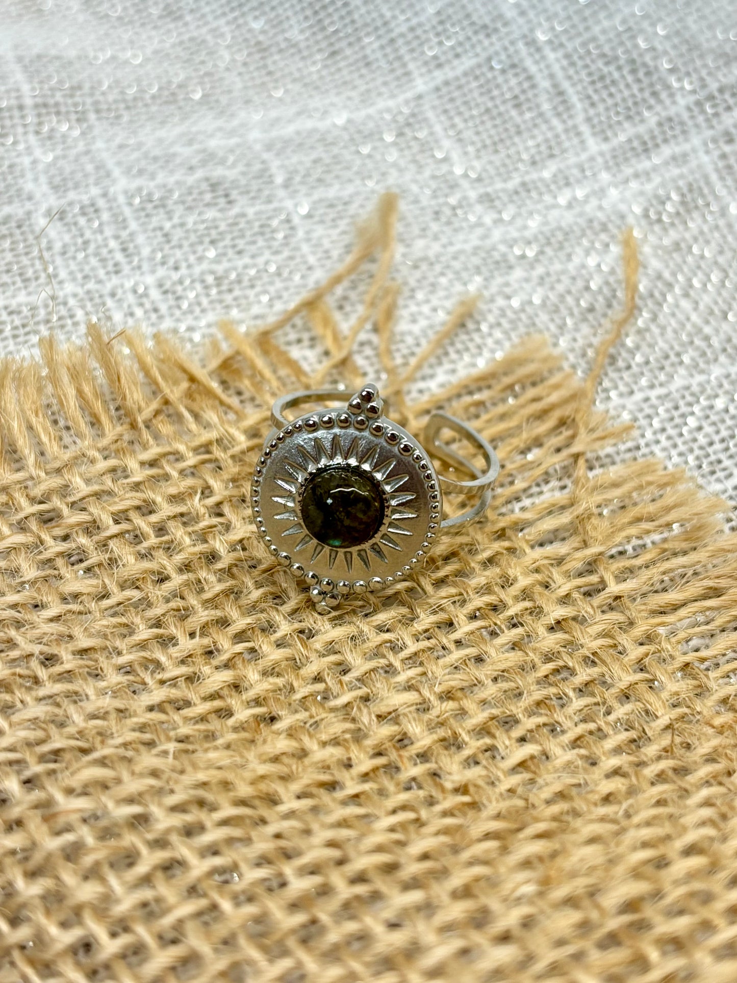 Bague ZÉLIE en acier inoxydable argent, avec pierre de Labradorite, exposé sur de la toile de jute et fond en lin blanc.