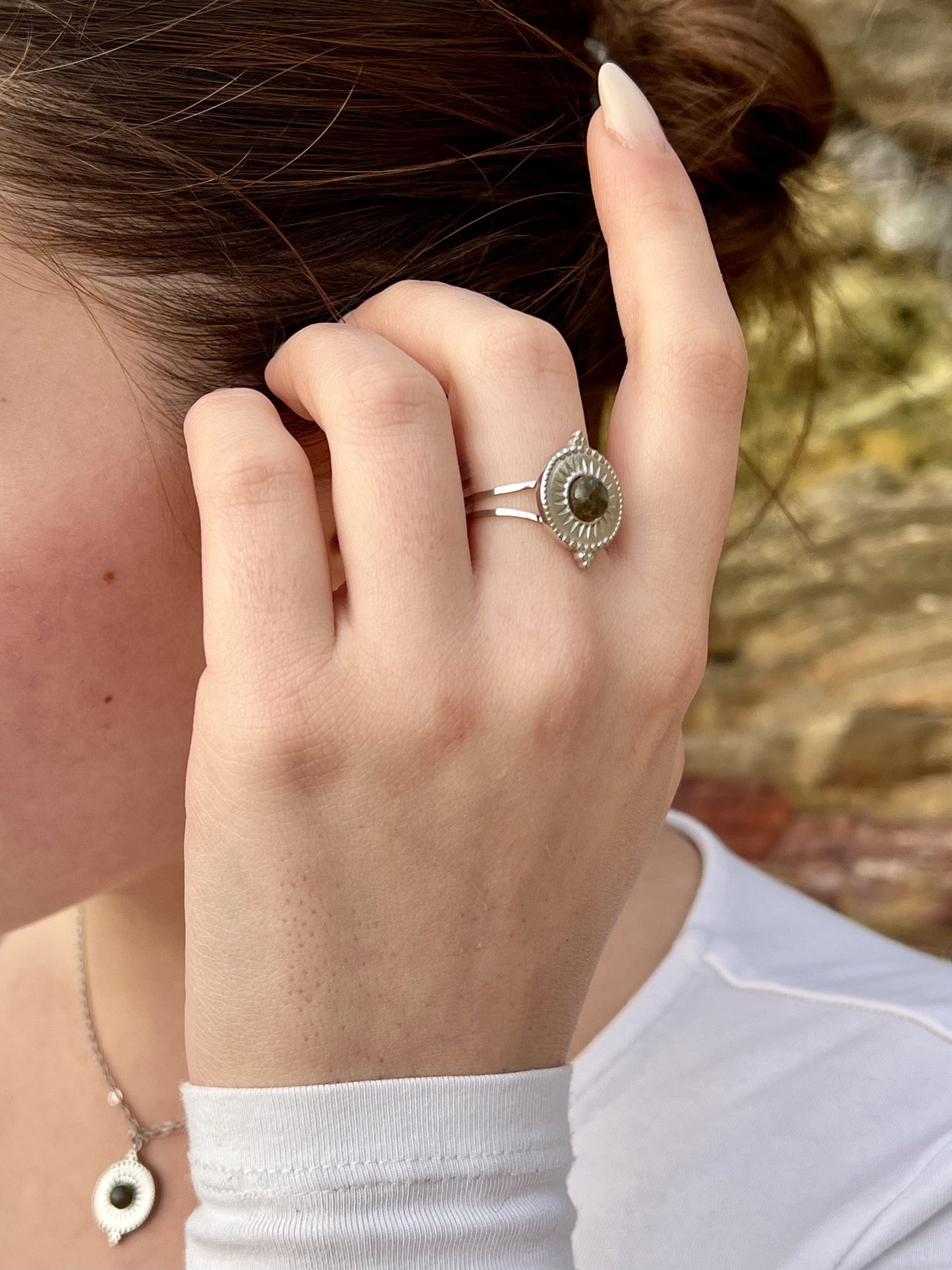 Bague et Collier ZÉLIE en acier inoxydable argent, avec pierre de Labradorite, portés par une femme dans les rochers.