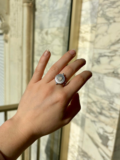 Bague ZÉLIE en acier inoxydable argent et Pierre de Lune, sur une main de femme avec un fond en marbre.