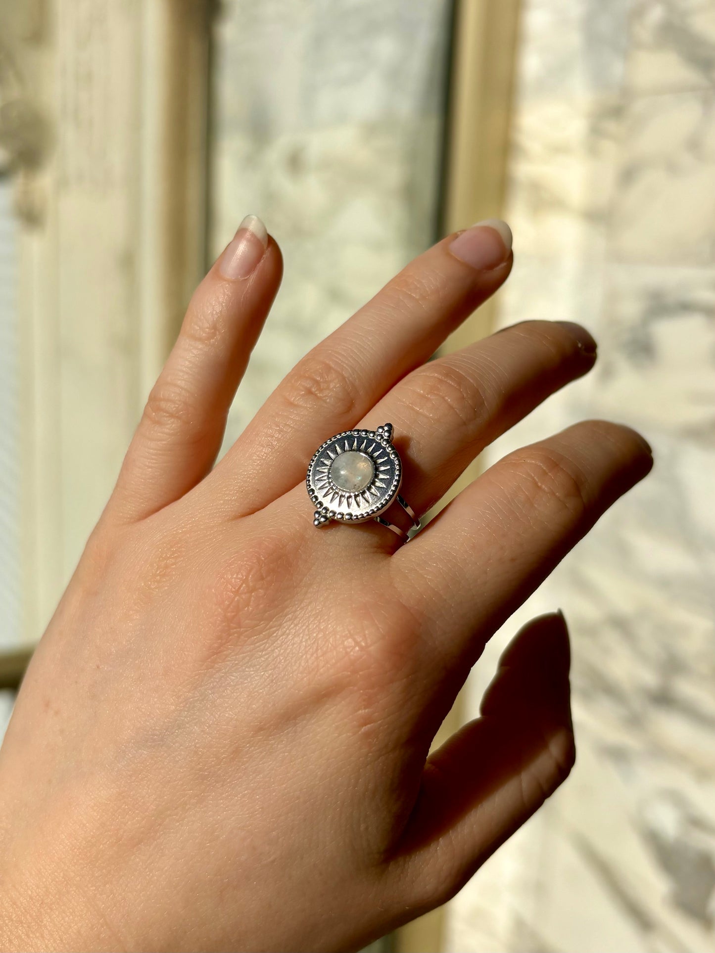 Bague ZÉLIE en acier inoxydable argent et Pierre de Lune, sur une main de femme avec un fond en marbre.