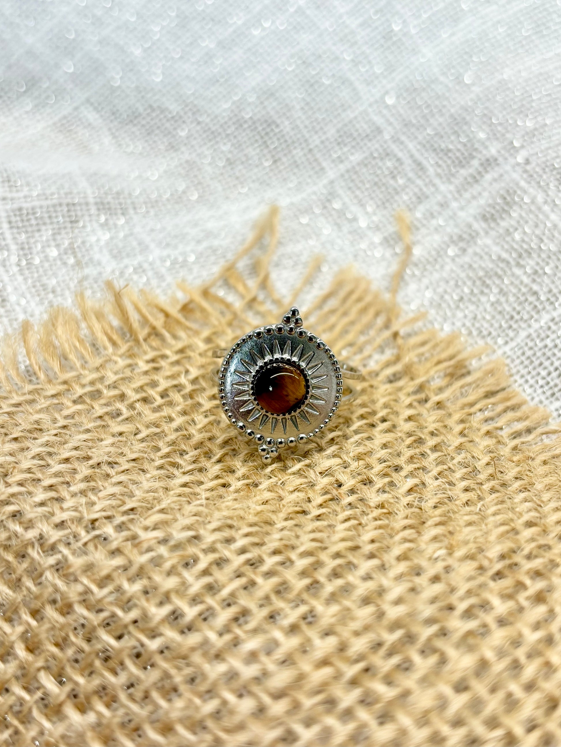 Bague ZÉLIE en acier inoxydable argent avec pierre d'oeil de tigre, exposé sur de la toile de jute et un fond en lin blanc.