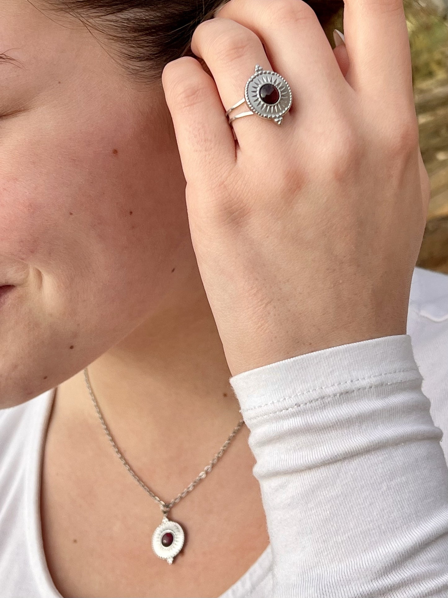 Collier et bague ZÉLIE en acier inoxydable argent et pierre de Grenat, porté par une fille sur les rochers.