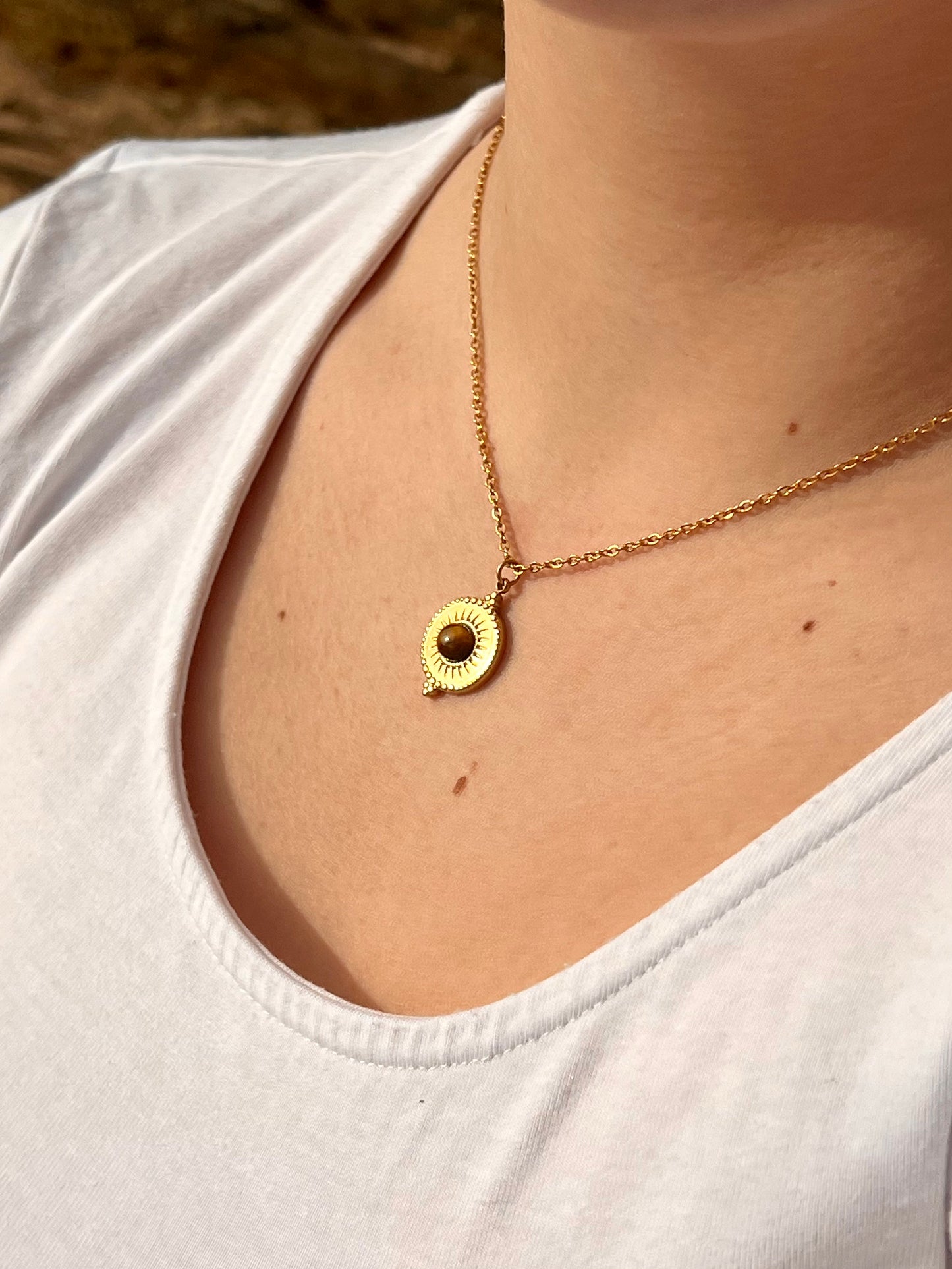 Collier ZÉLIE en acier inoxydable doré et pierre d'oeil de tigre, porté par une fille dans les rochers